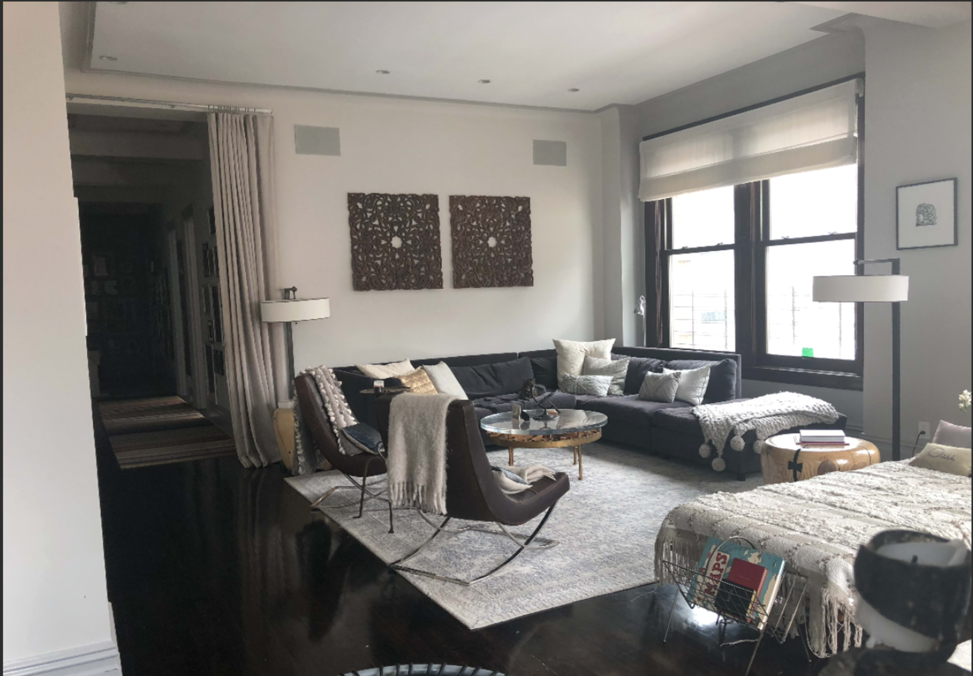 A modern living room features a sectional sofa, a round coffee table, and artwork on the walls, with large windows allowing natural light to enter.
