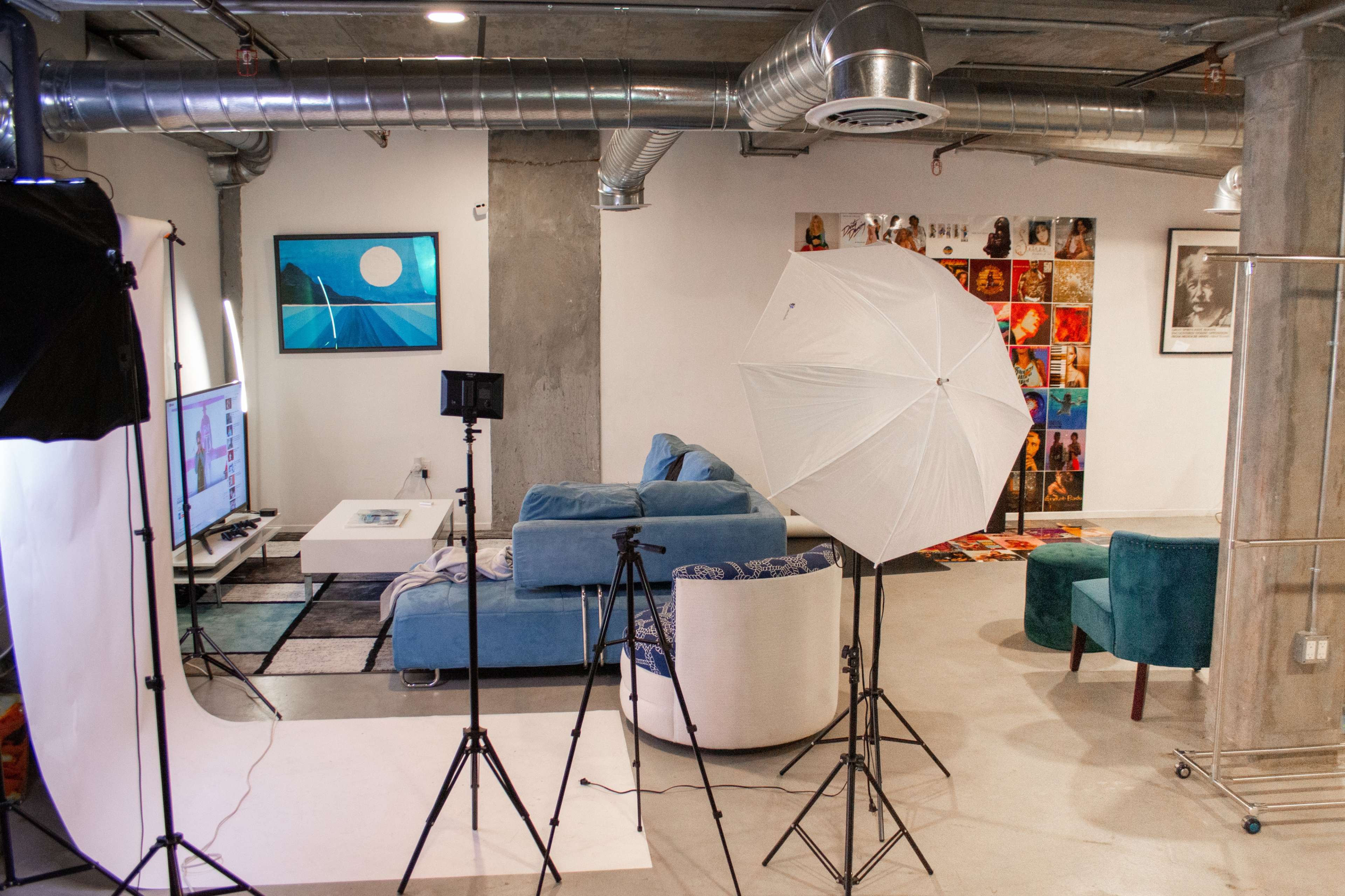 A modern living space with a blue sofa, a television, and various photography equipment set up, including a light umbrella and tripods.