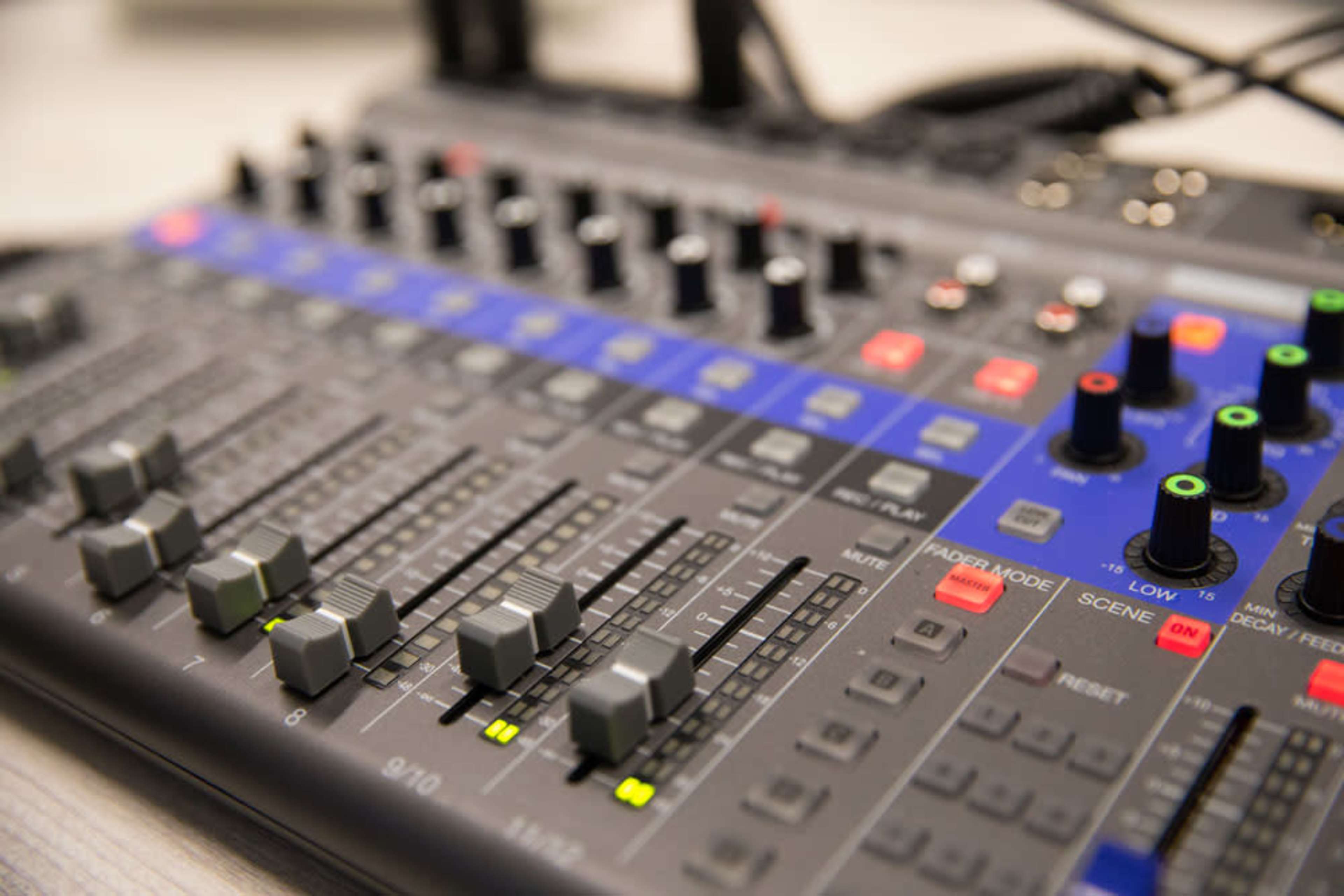 A close-up of an audio mixing console with various sliders, buttons, and knobs arranged in a grid layout.