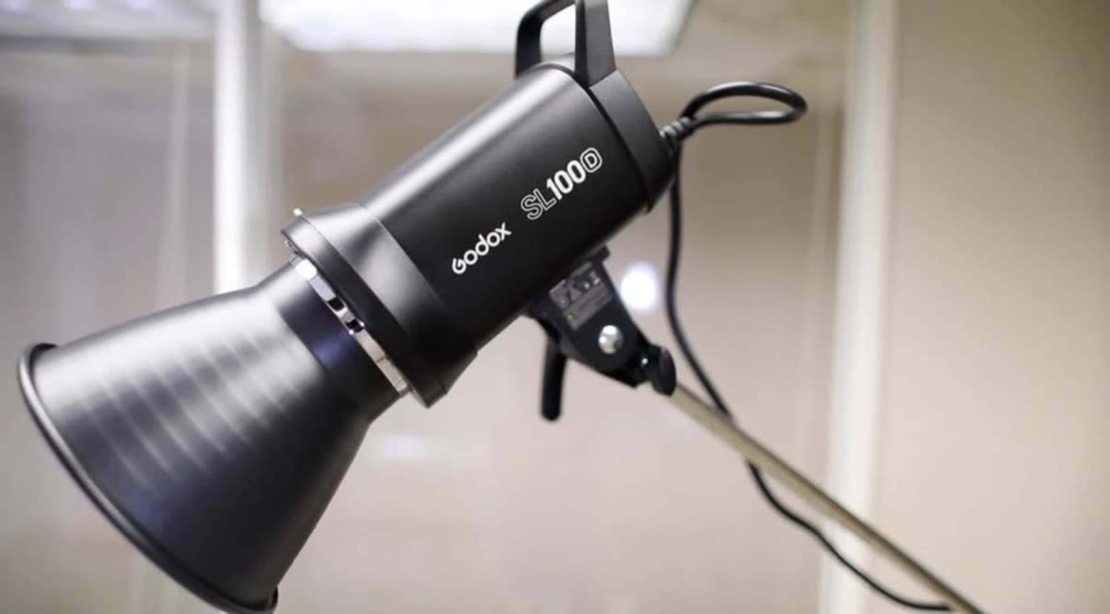 The image shows a Godox SL100W studio light mounted on a stand, featuring a reflective cone and a power cable.