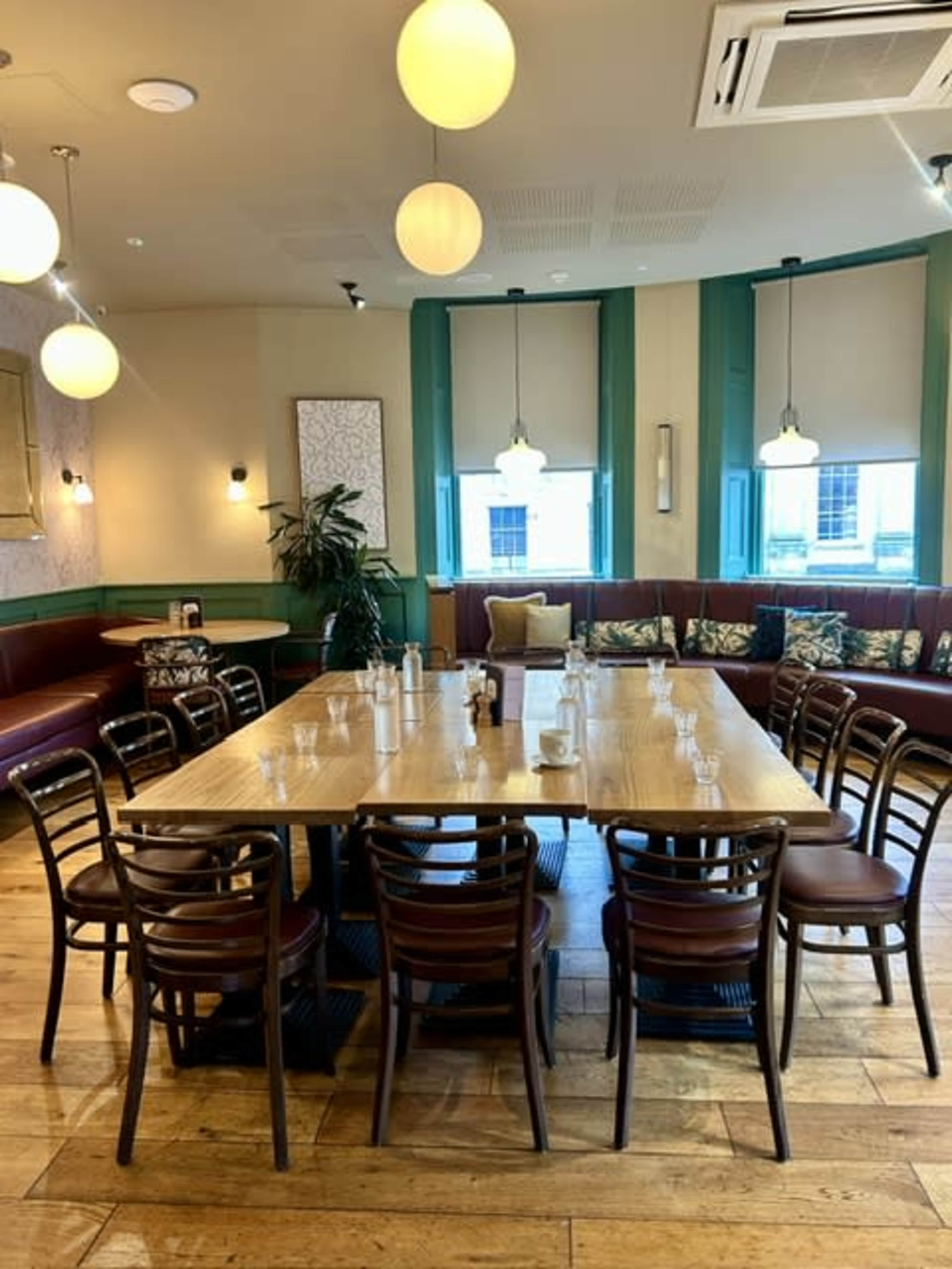 A large wooden table surrounded by chairs is set up in a well-lit dining area featuring green and beige decor.