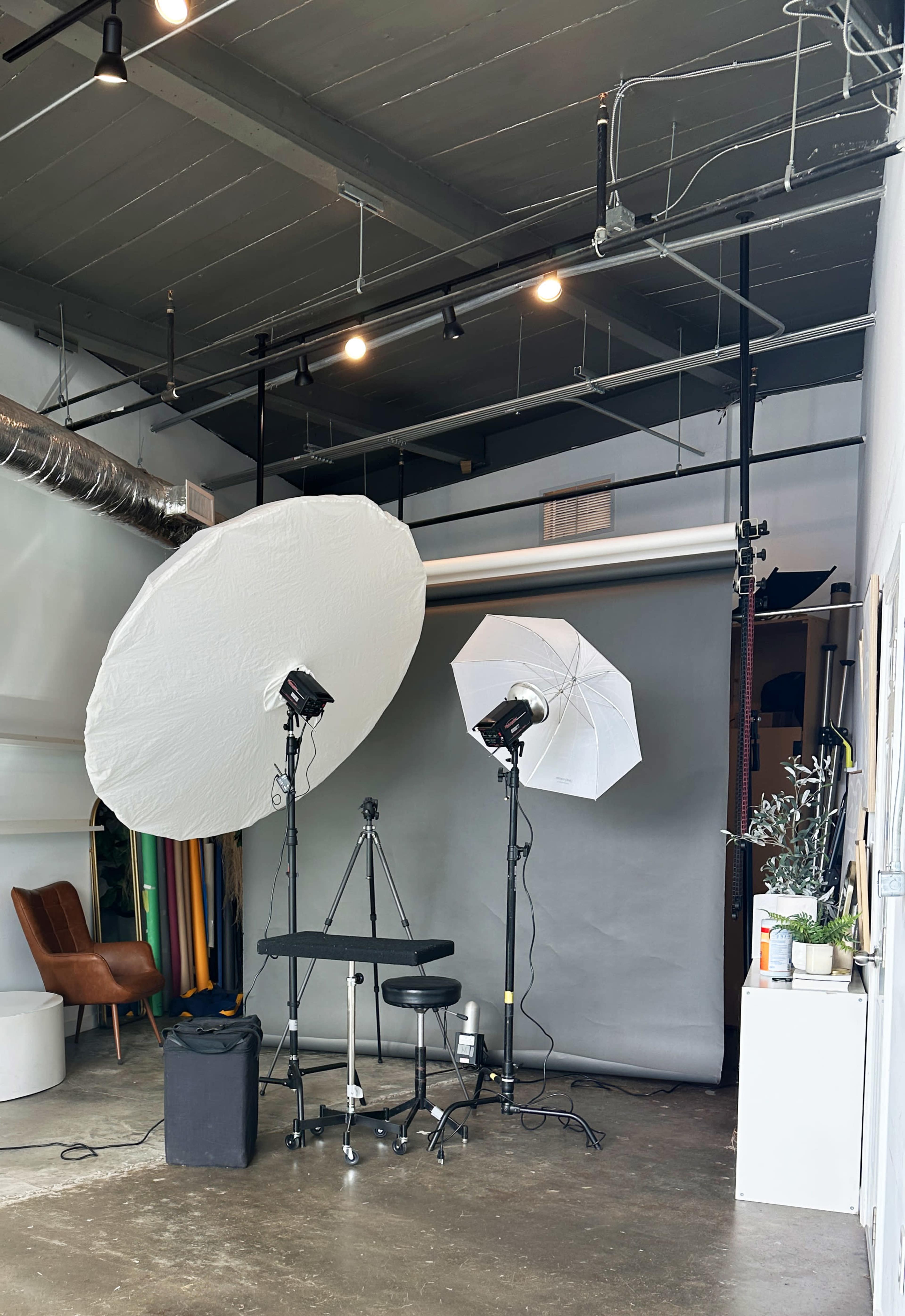 The image shows a photography studio setup with two large softbox lights, a stool, and a backdrop in a neutral color.