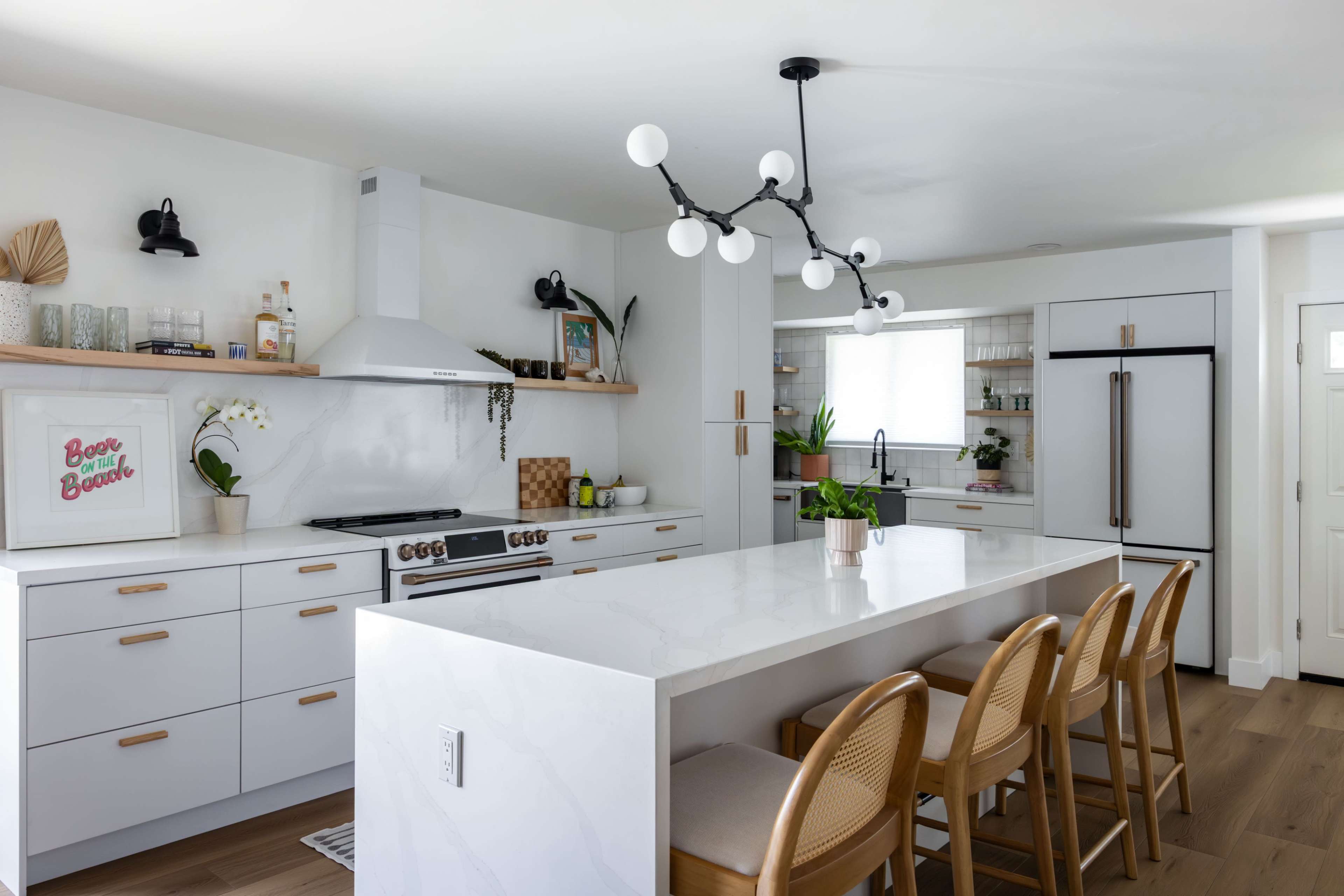 The image shows a modern kitchen featuring a white island with seating, sleek cabinetry, a gas range, and a unique light fixture above the island.