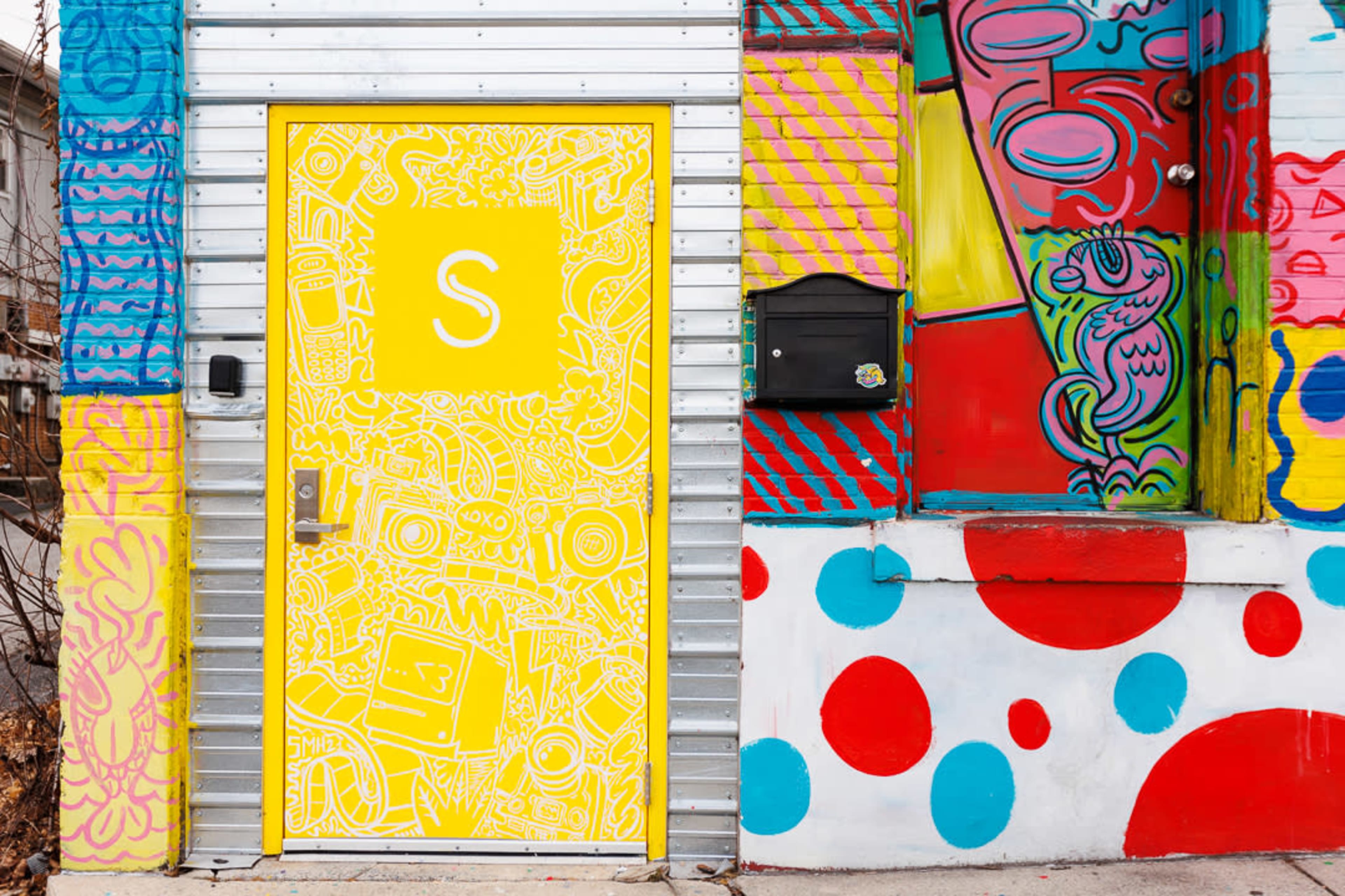 A vibrant mural on a building with a bright yellow door, adorned with intricate line drawings and surrounded by colorful abstract patterns.