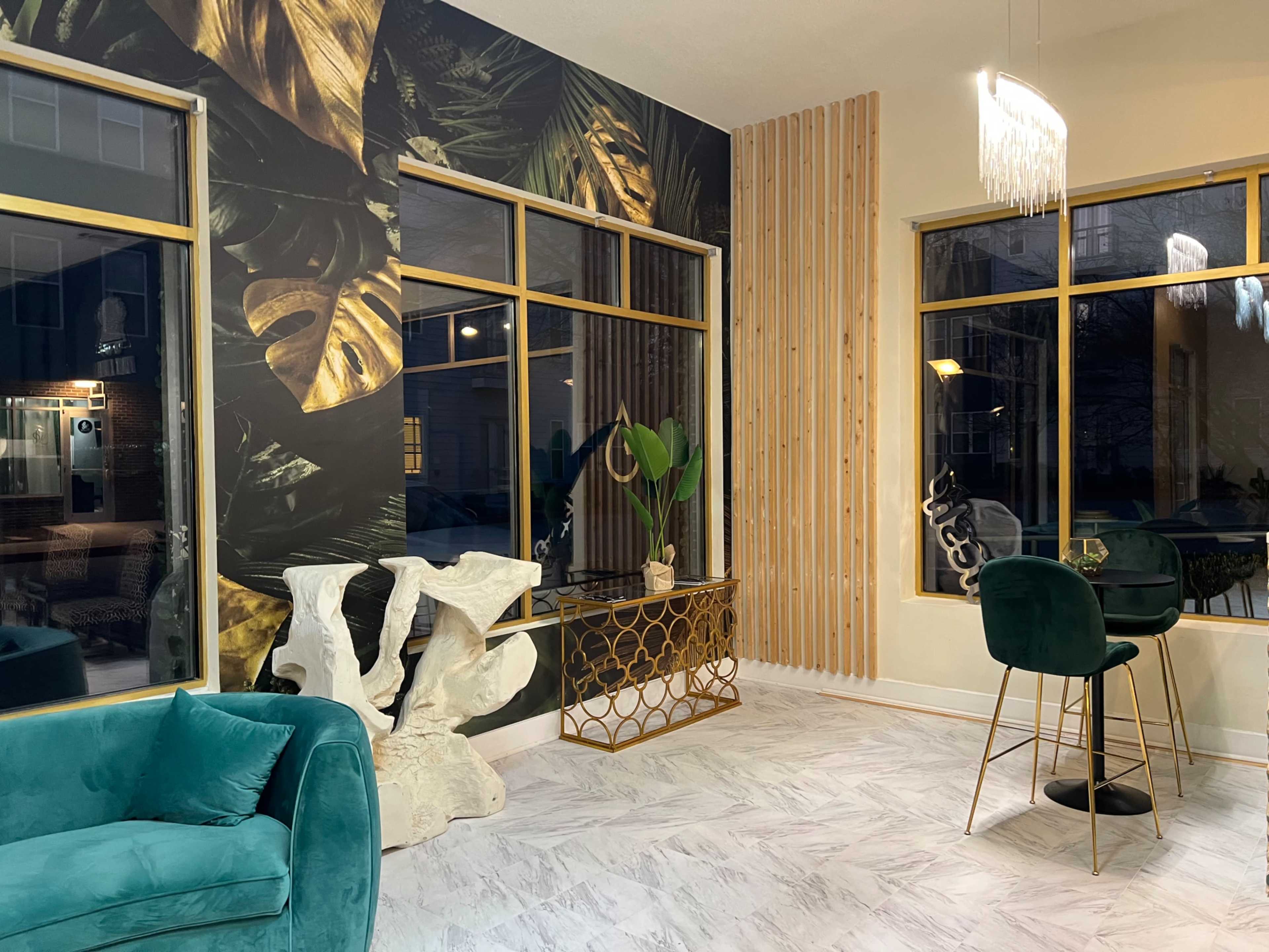 A modern lounge area with green and gold decor, featuring a decorative plant, a sculptural piece, and large windows providing natural light.