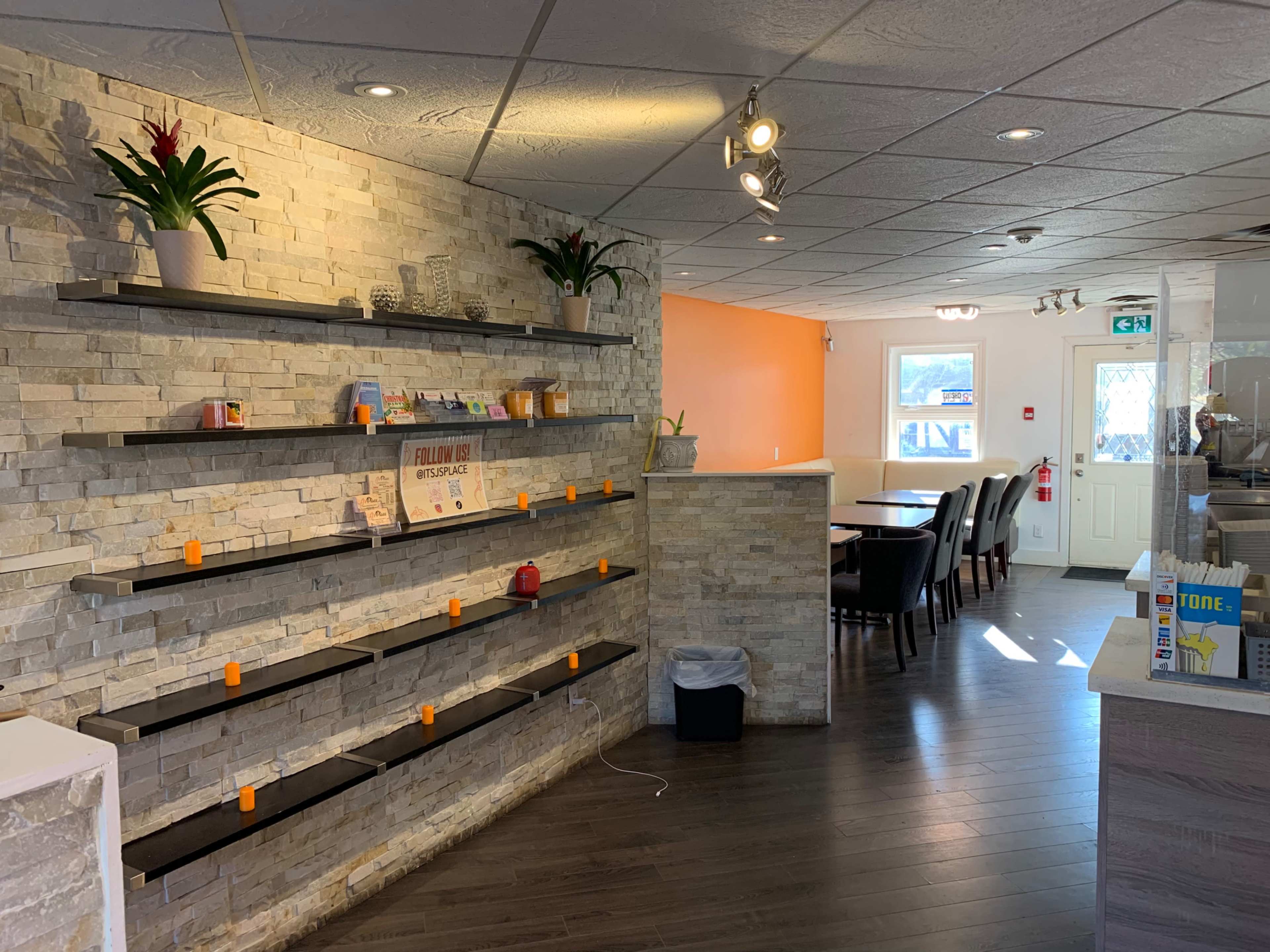 A modern reception area with a textured stone wall, floating shelves displaying items, and a dining area in the background.