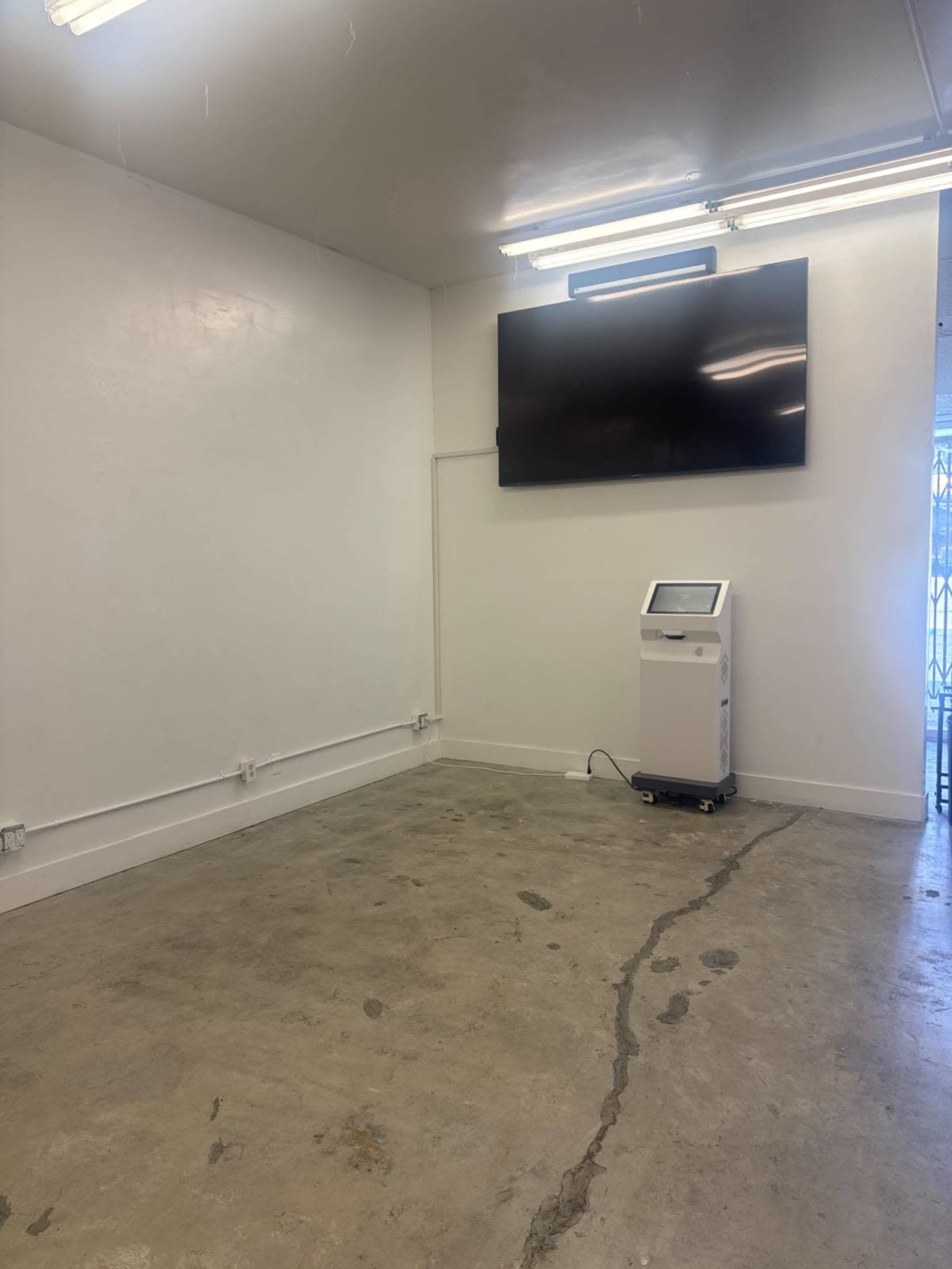 A bare room with concrete flooring, a wall-mounted television, and a standing kiosk.