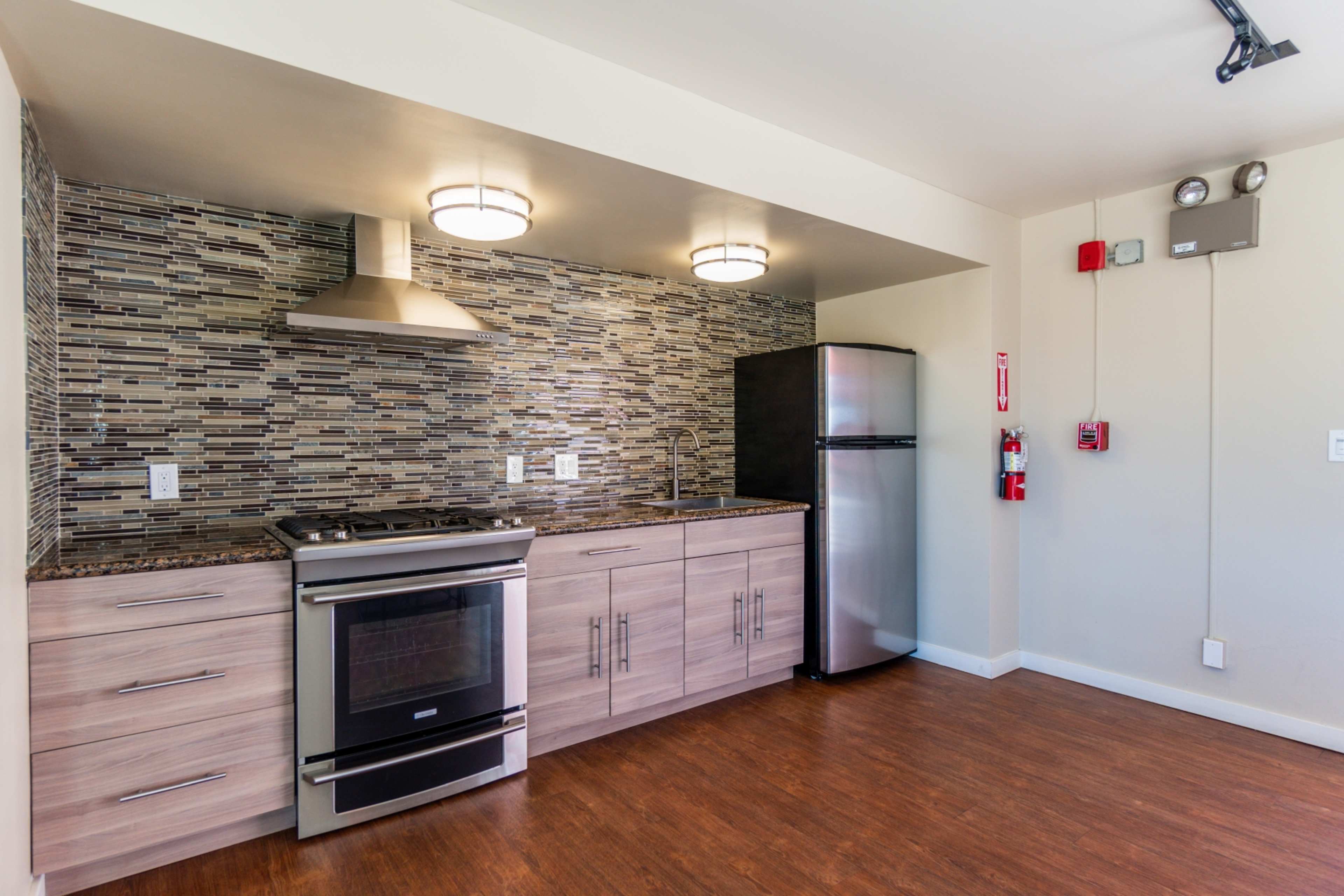 The image shows a modern kitchen with stainless steel appliances, including a refrigerator and oven, set against a mosaic tile backsplash.