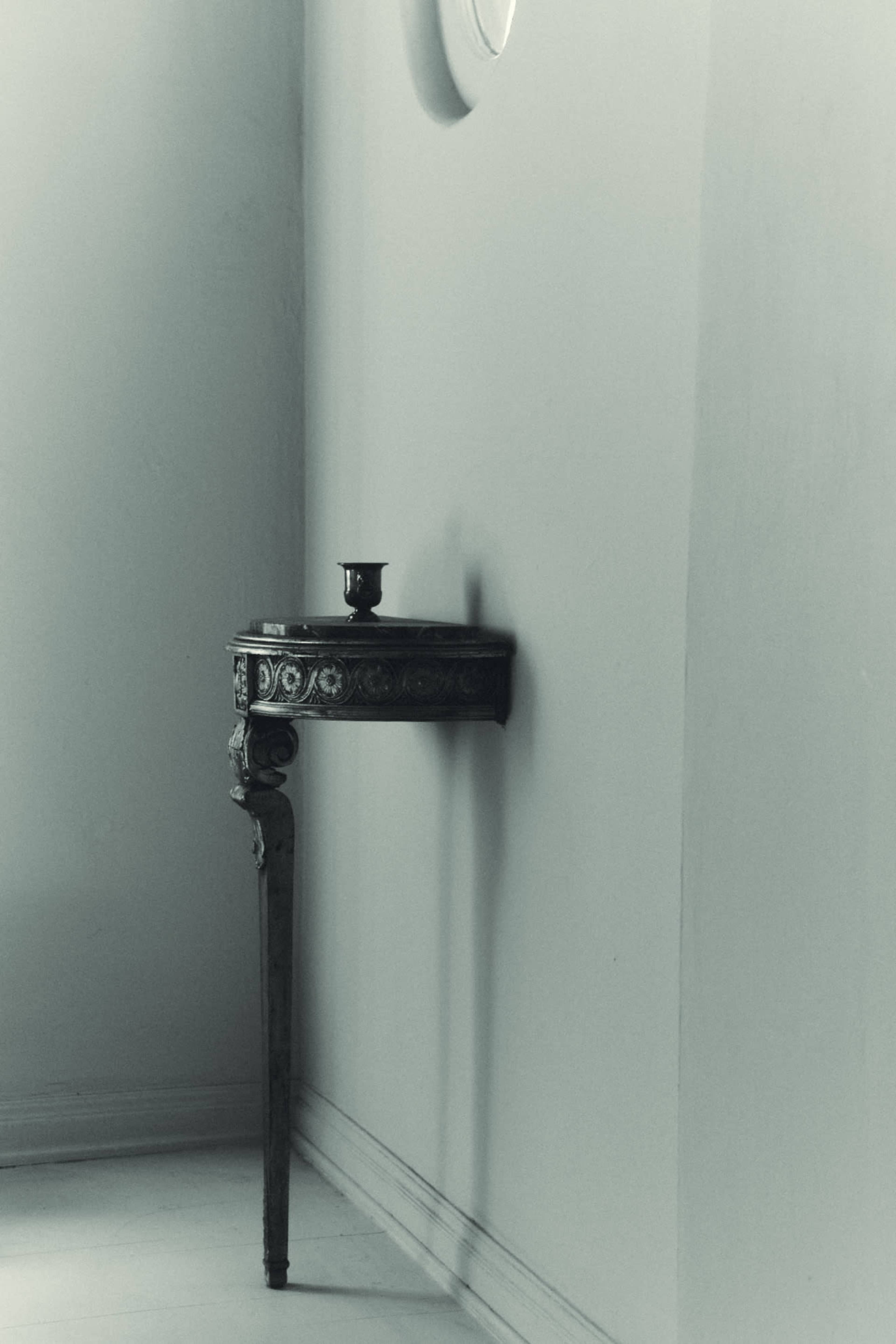 A small, decorative side table is positioned against a wall, with a single metal cup placed on top.