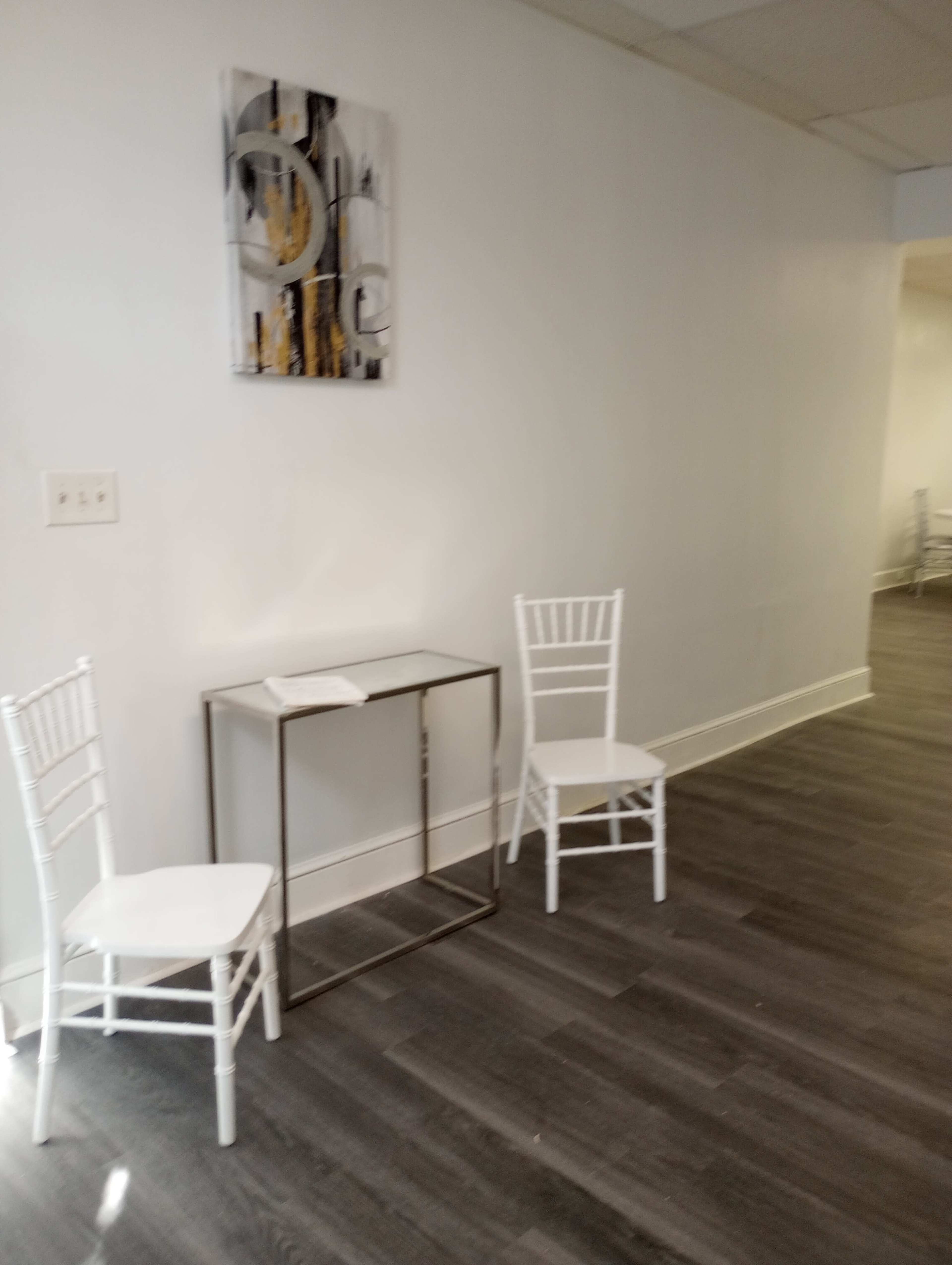 A minimalistic interior space with two white chairs and a small table against a light-colored wall.