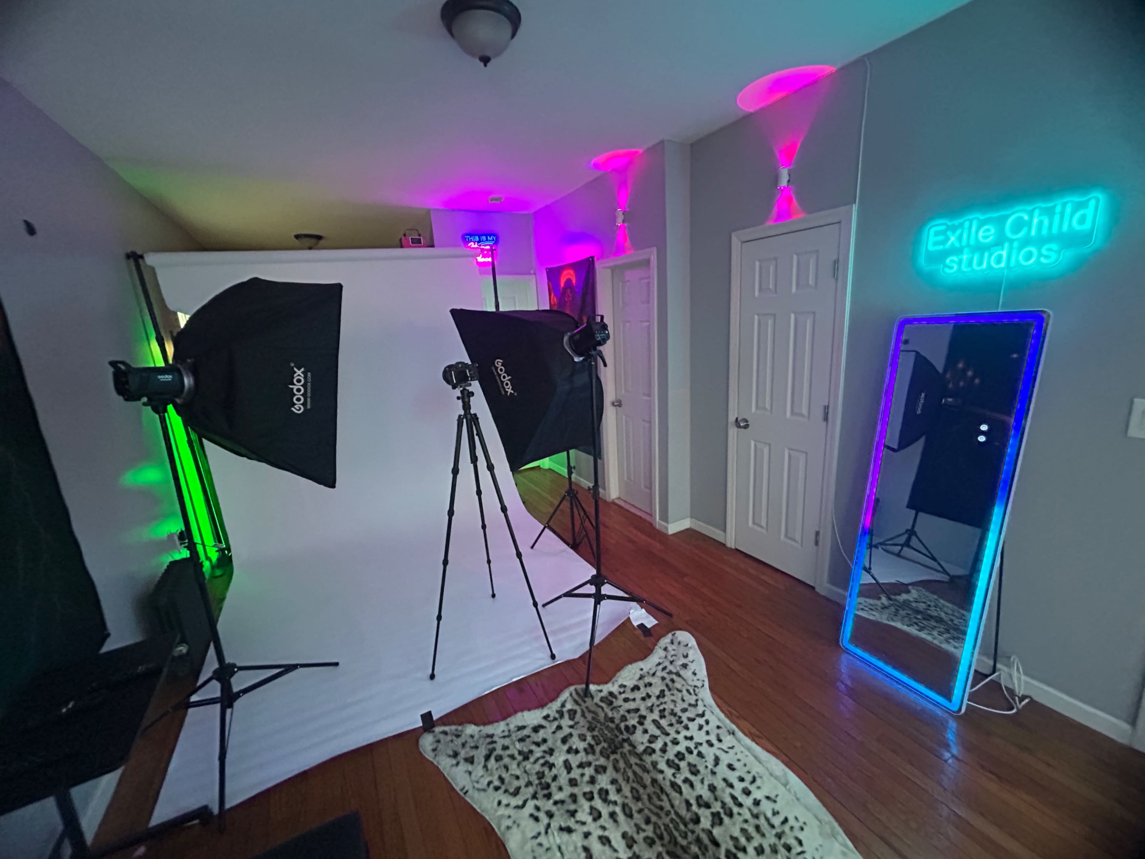 The image shows a photography studio setup featuring two softbox lights, a white backdrop, a full-length mirror, and colorful ambient lighting.