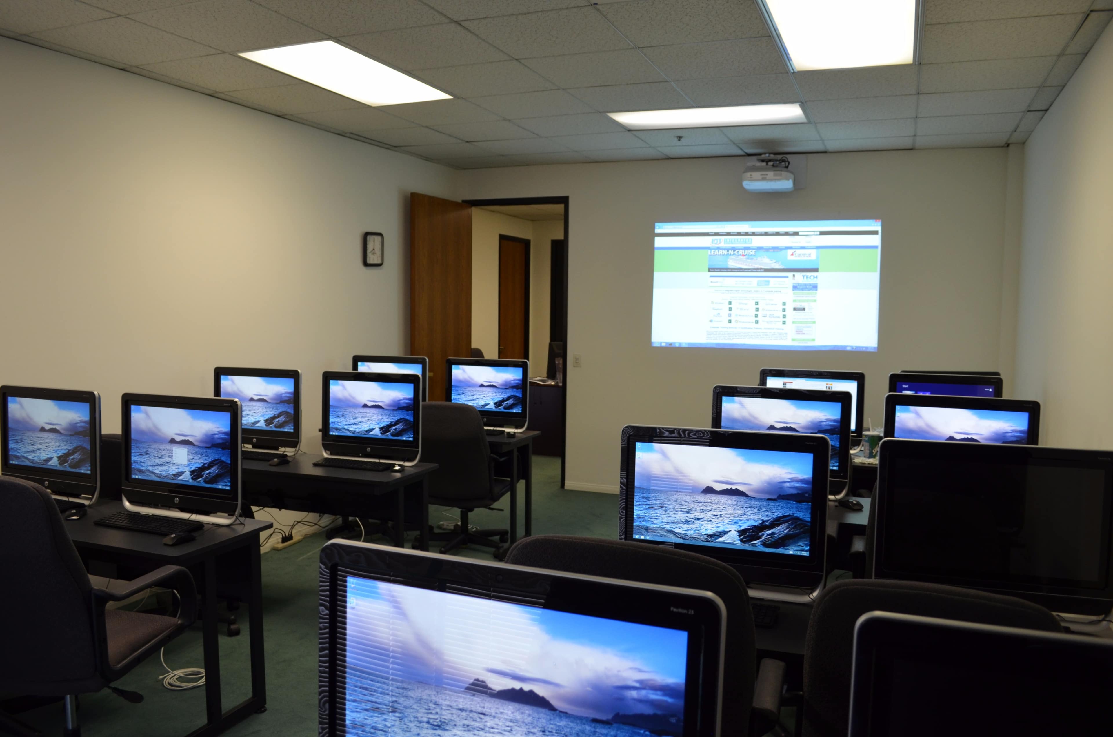 A computer lab with several desktop computers arranged in rows, displaying ocean images, and a projector screen showing a website.