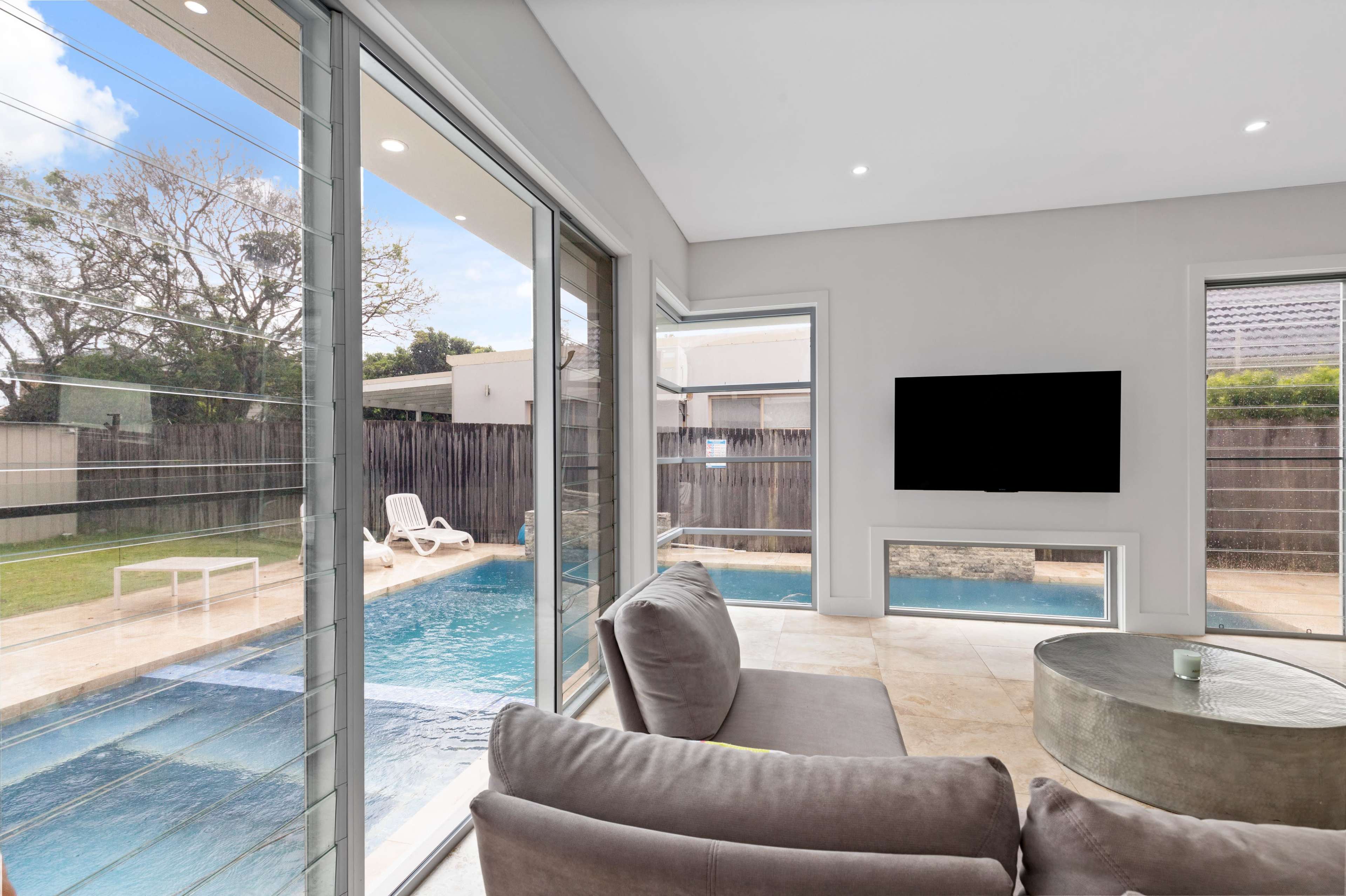 A modern living room with large windows overlooks a swimming pool and backyard area.