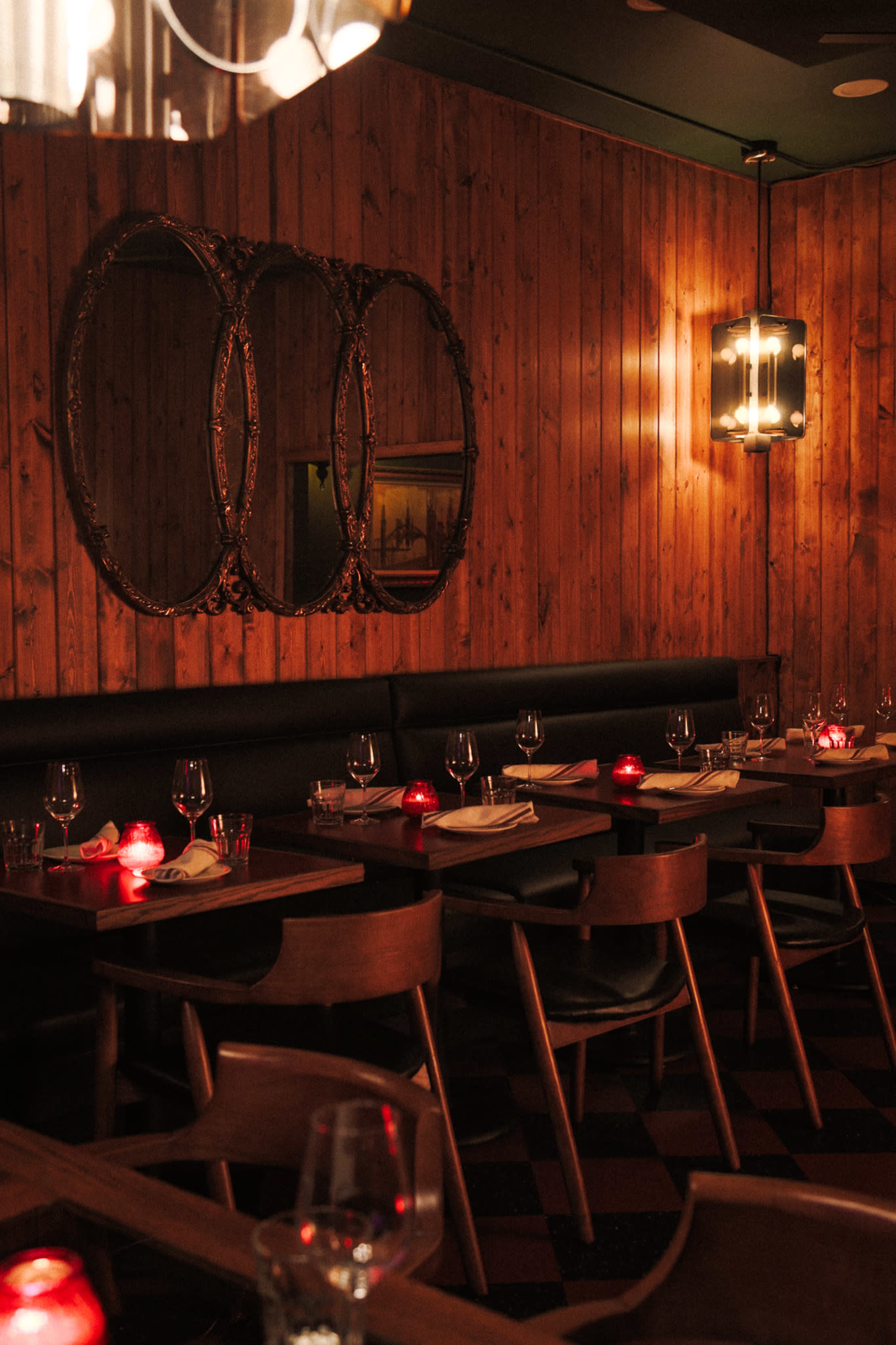 The image shows a dimly lit restaurant with wooden paneling, round mirrors on the wall, and tables set with wine glasses and red candles.