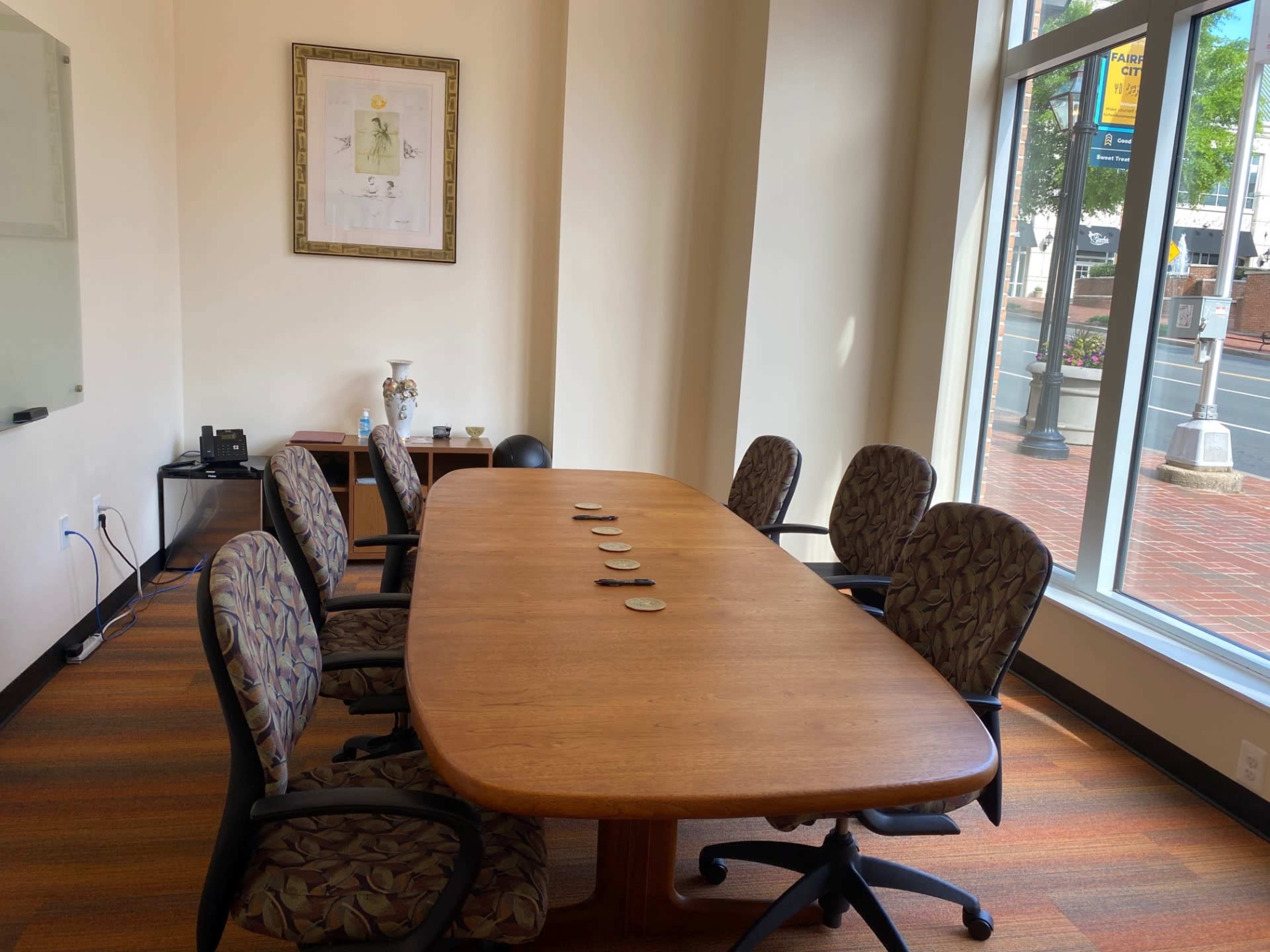 A conference room features a large wooden table with six patterned chairs arranged around it, and a whiteboard is visible on one wall.