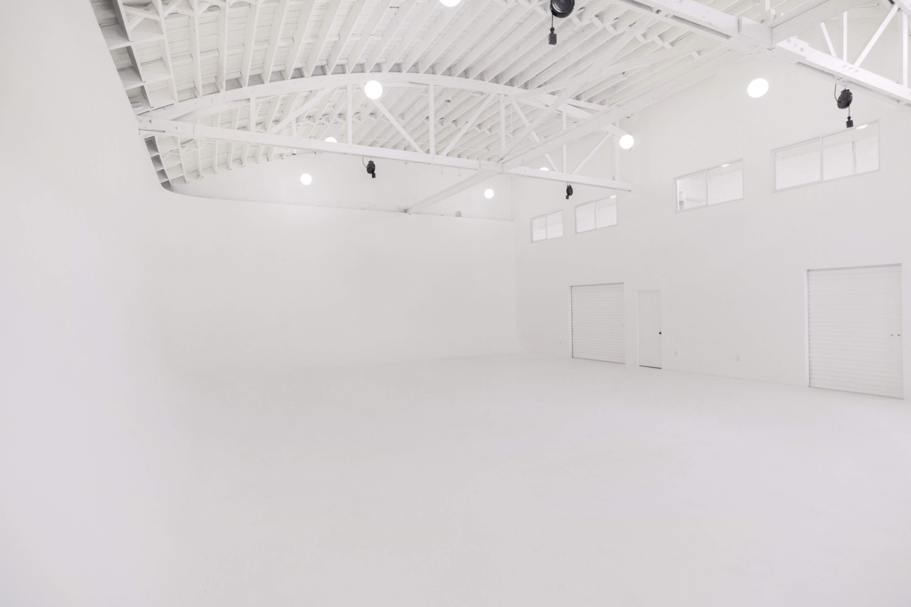 A spacious, empty white room with high ceilings and several windows.