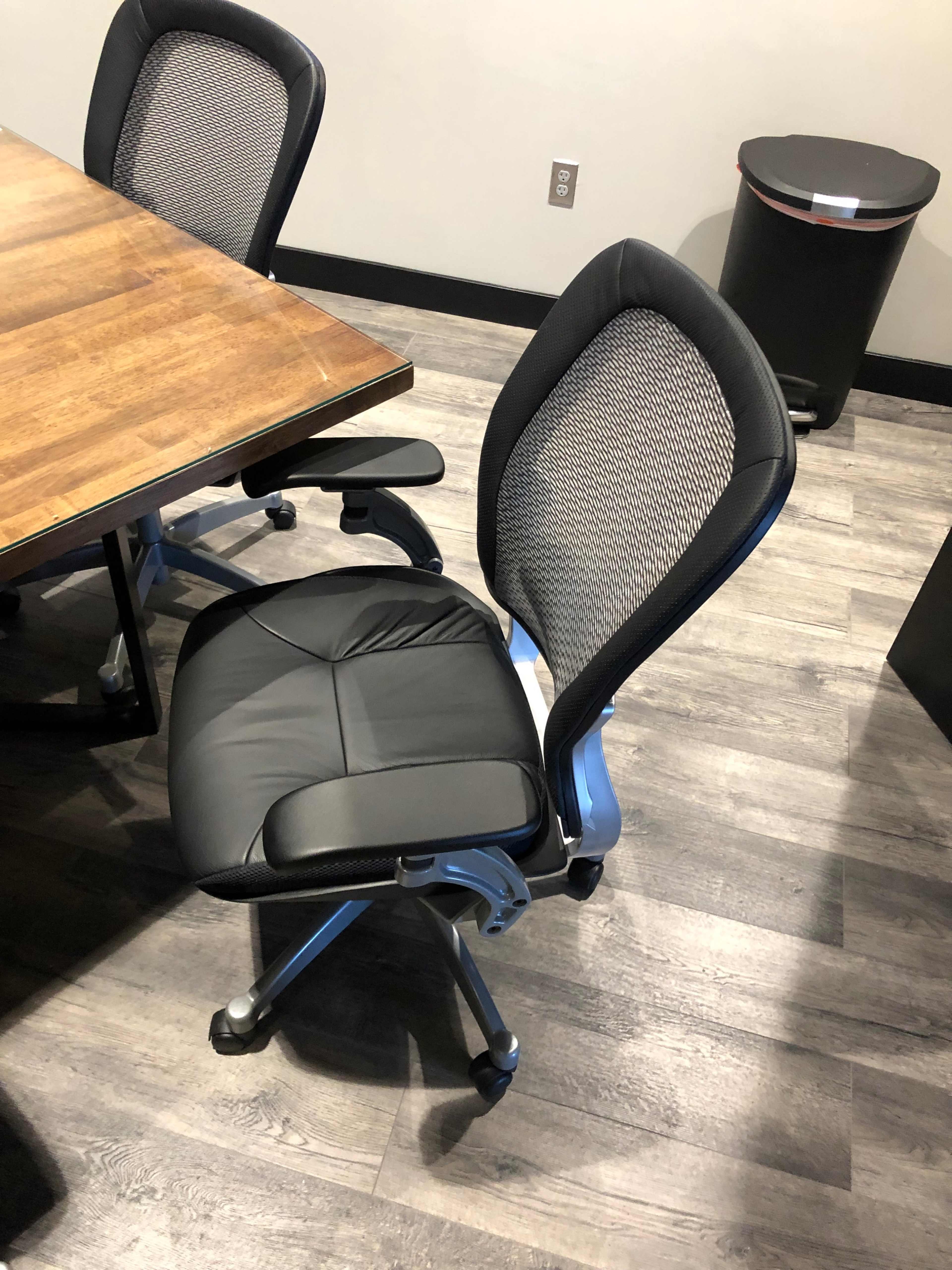 A black office chair with a mesh back, positioned next to a wooden table in an office setting.
