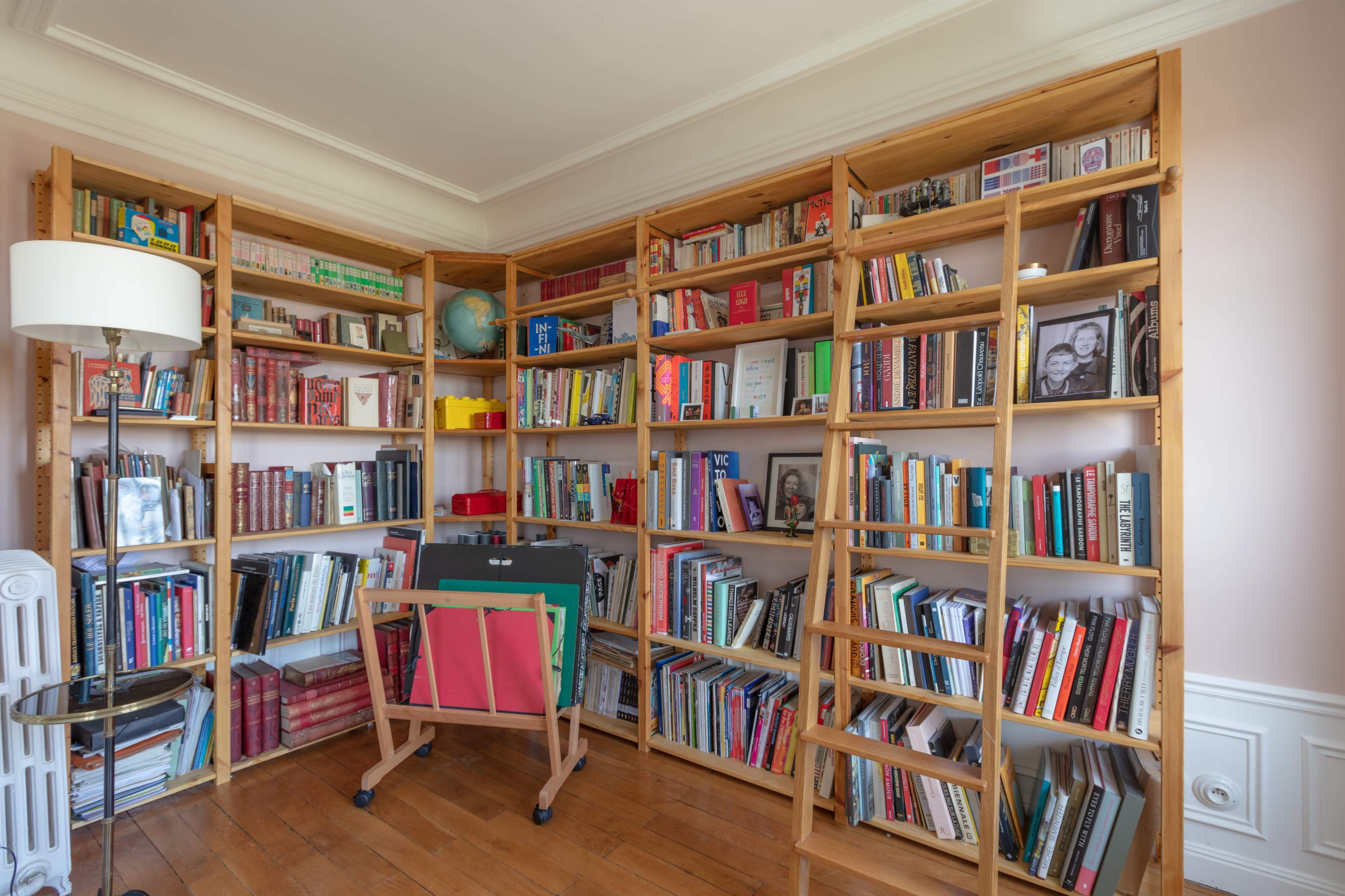 The image shows a room filled with wooden bookshelves neatly arranged with various books and a small folding table in front.