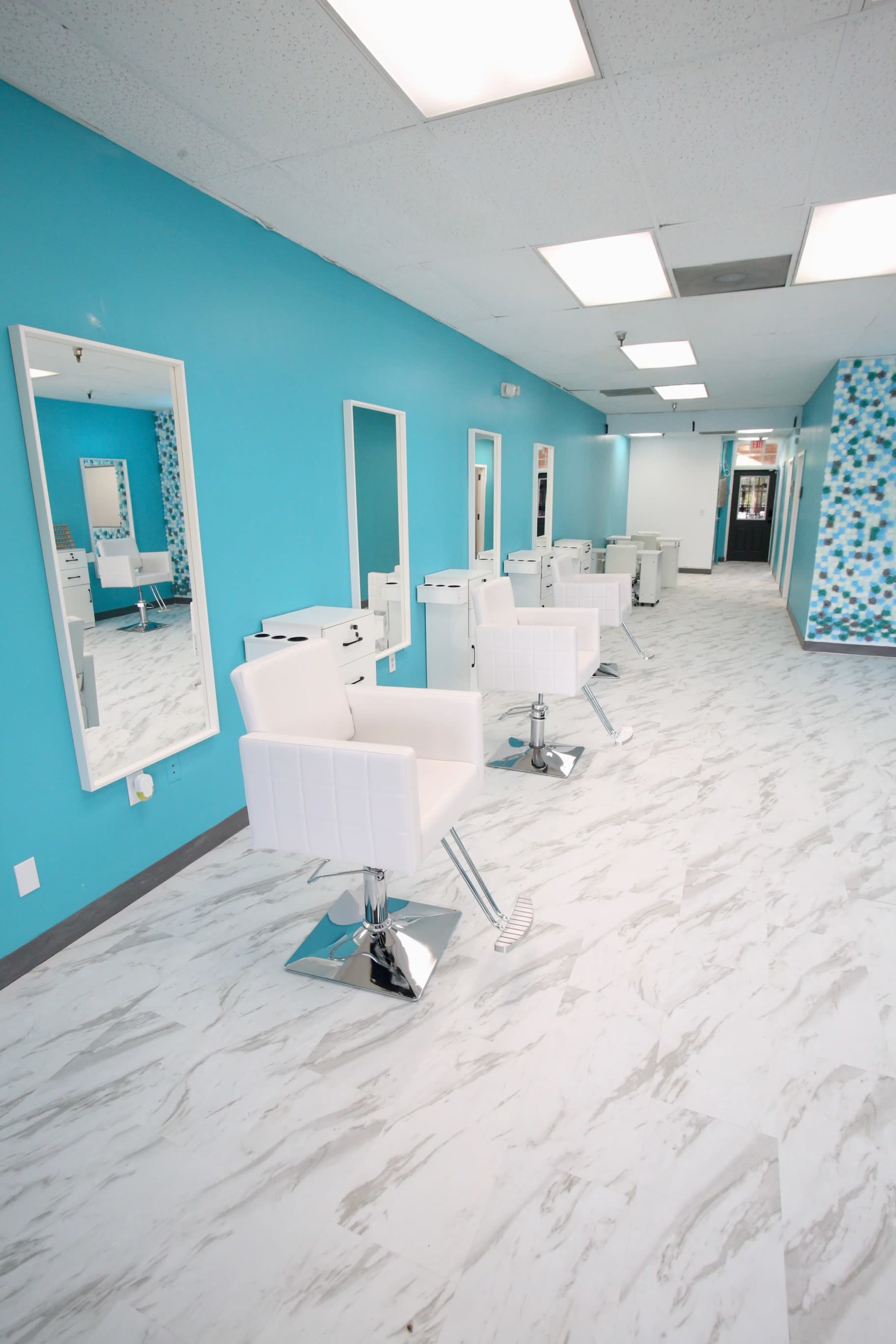 A brightly lit hair salon with white styling chairs and teal walls.