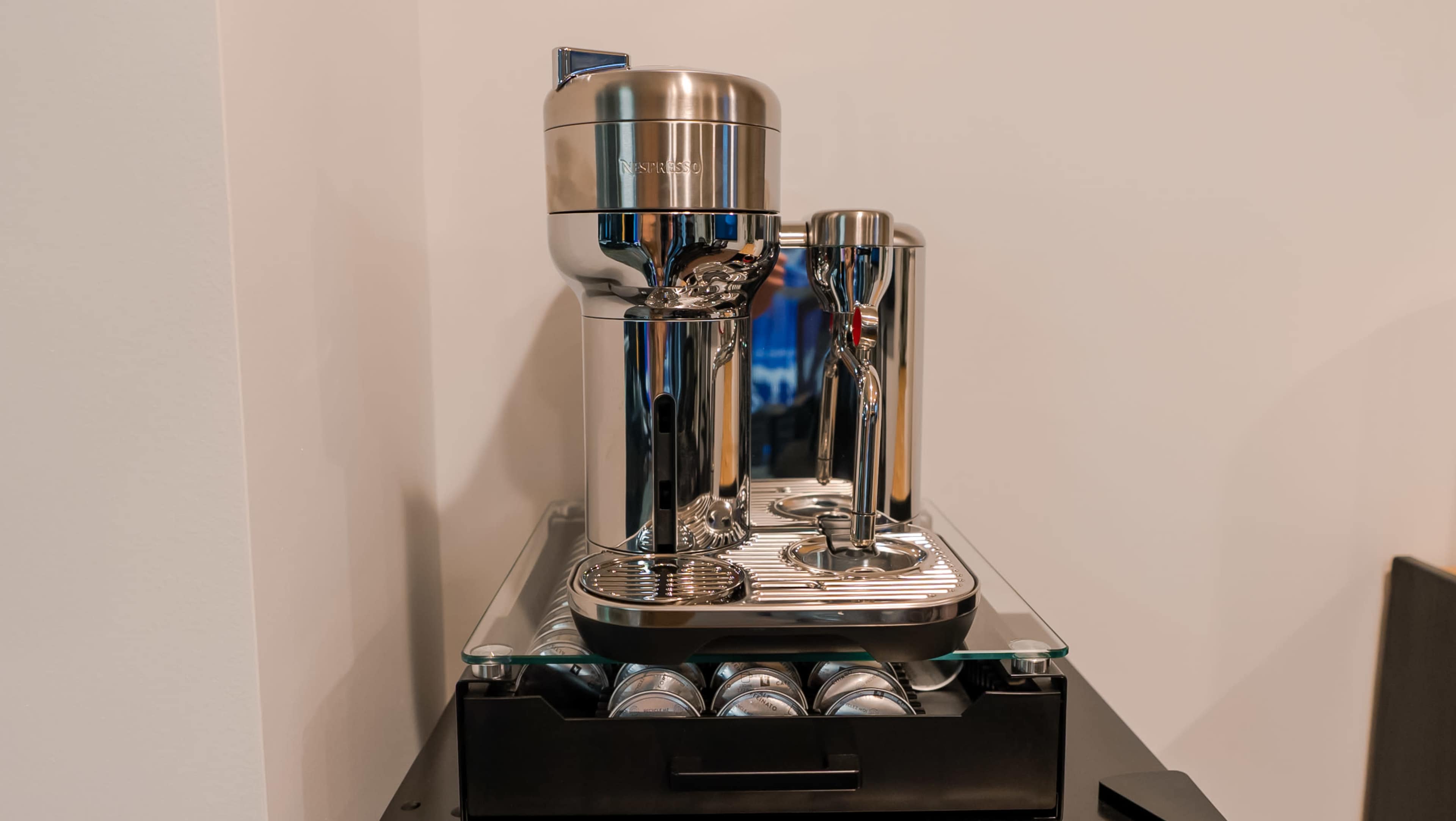 A sleek, chrome espresso machine positioned on a black countertop with a glass surface.
