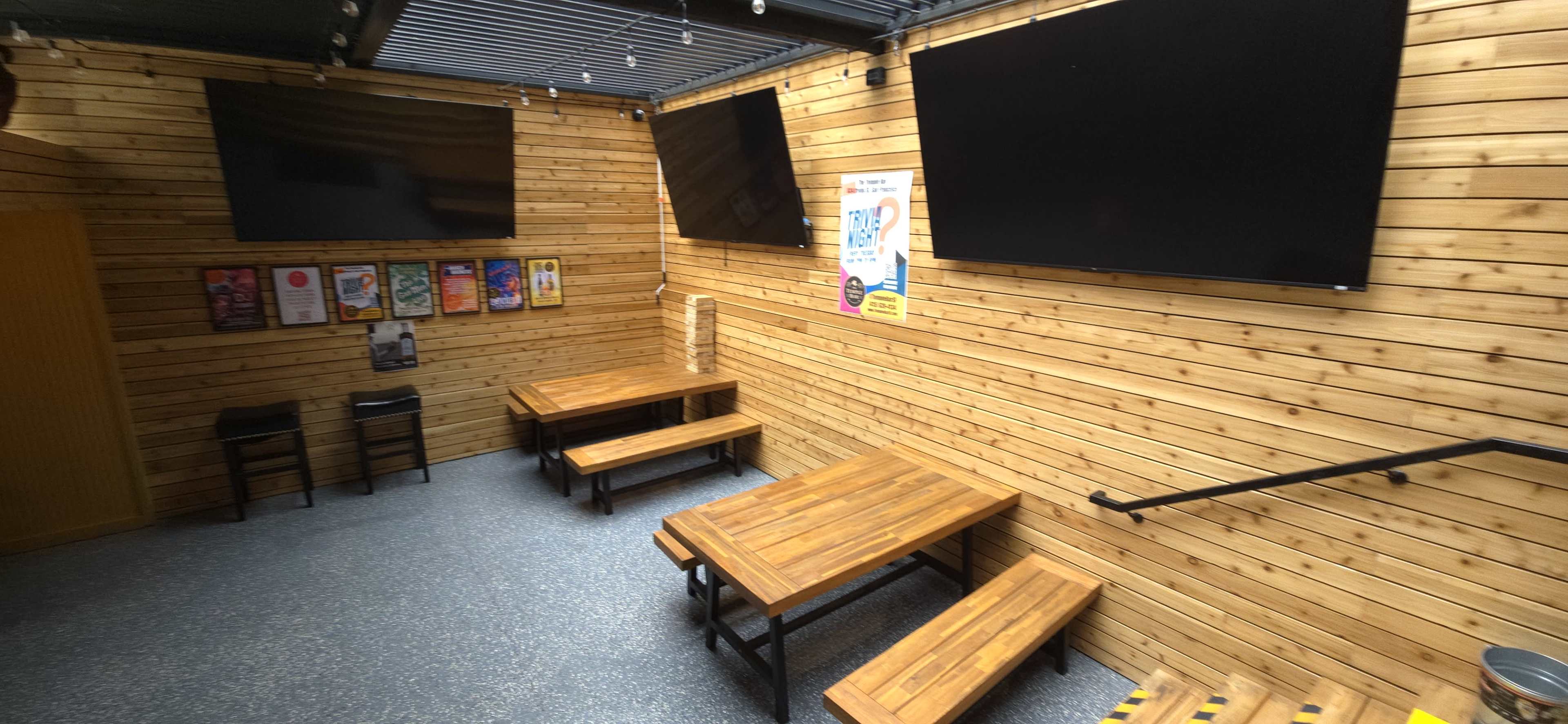 The image shows a wooden-paneled room with two large wall-mounted screens and several wooden tables and benches arranged inside.