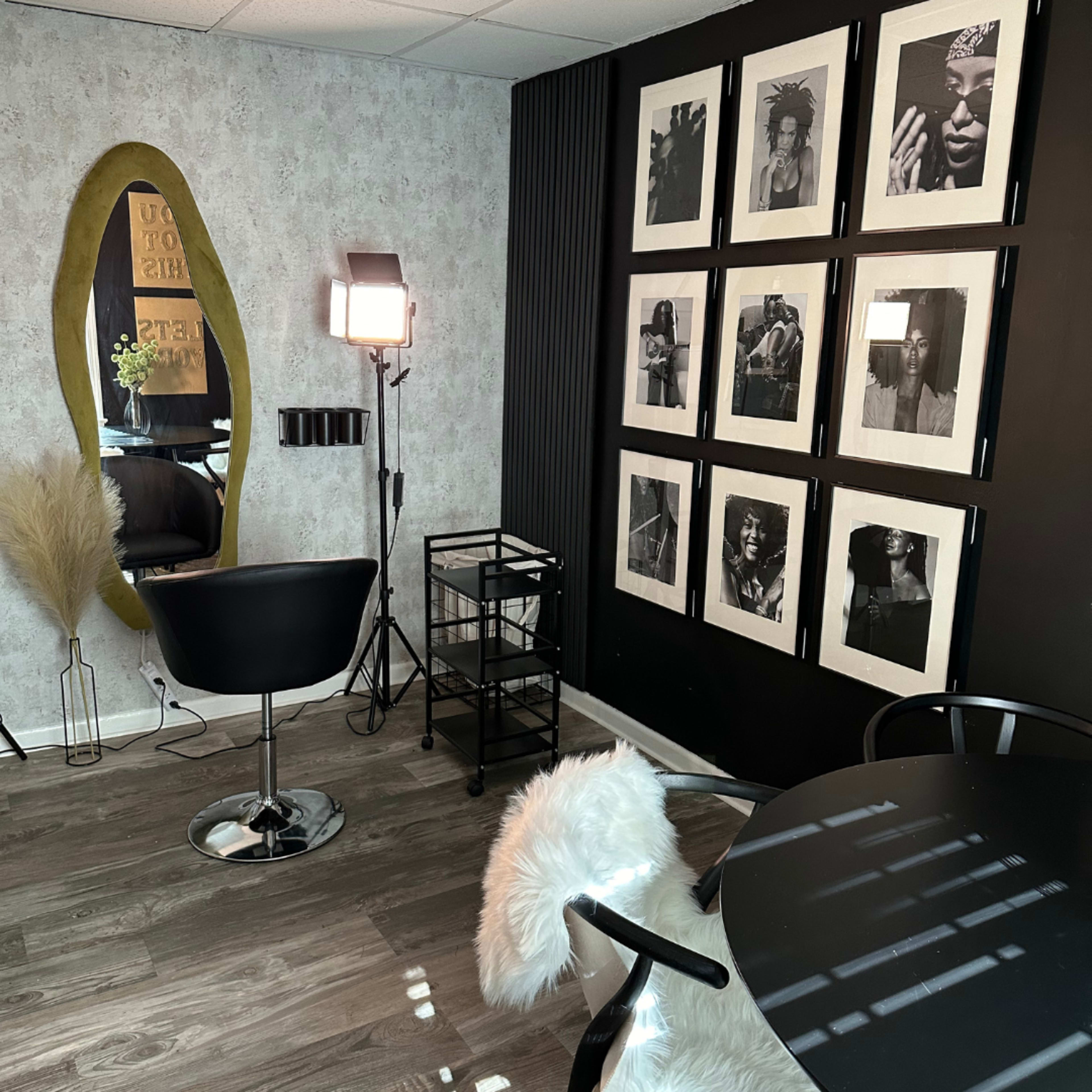 A modern room with a black wall displaying framed black-and-white photos, a large mirror, a hair styling chair, and a small cart.