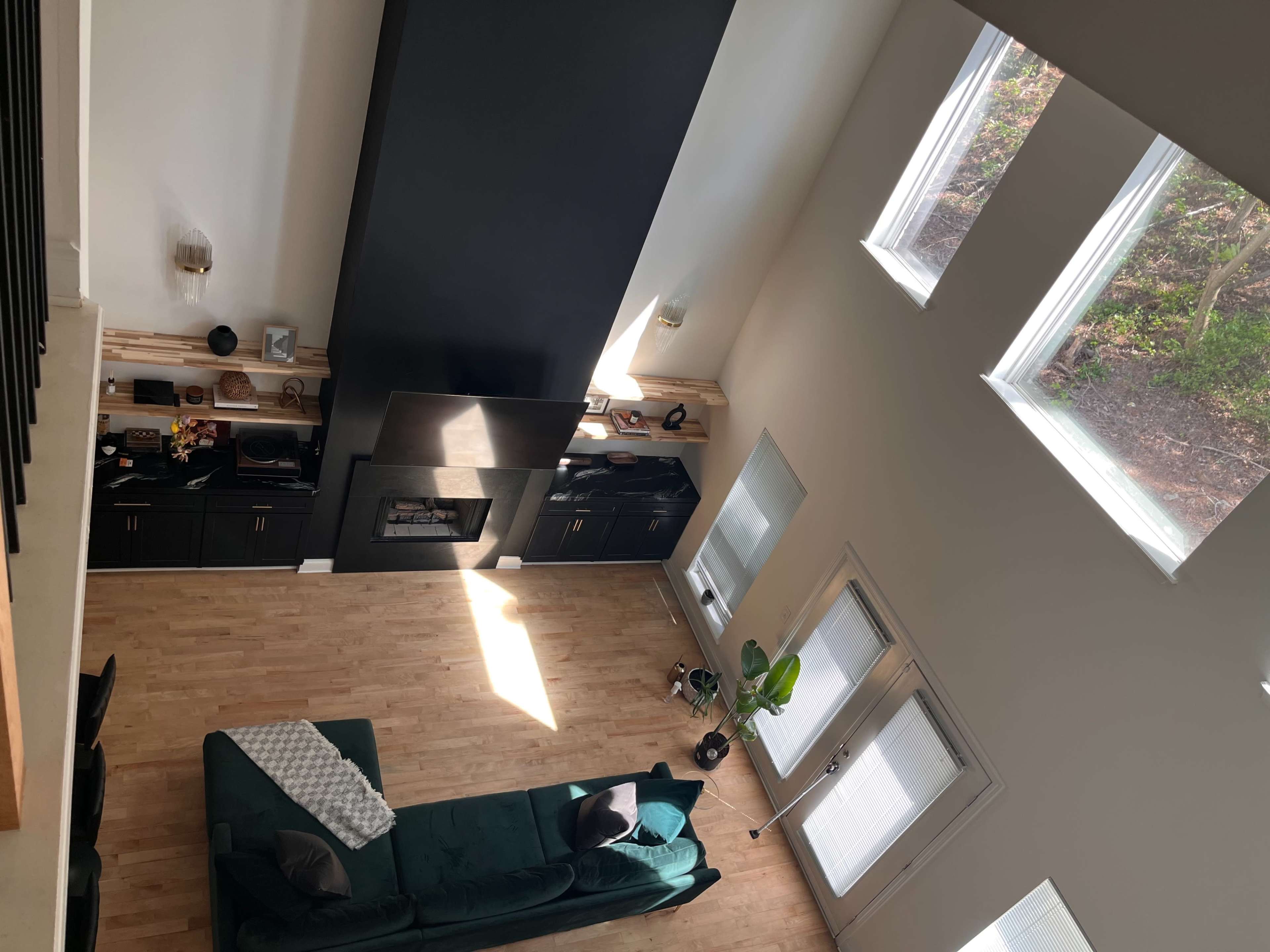 An aerial view of a living room with a large black fireplace, a green sofa, and multiple windows allowing natural light to enter.