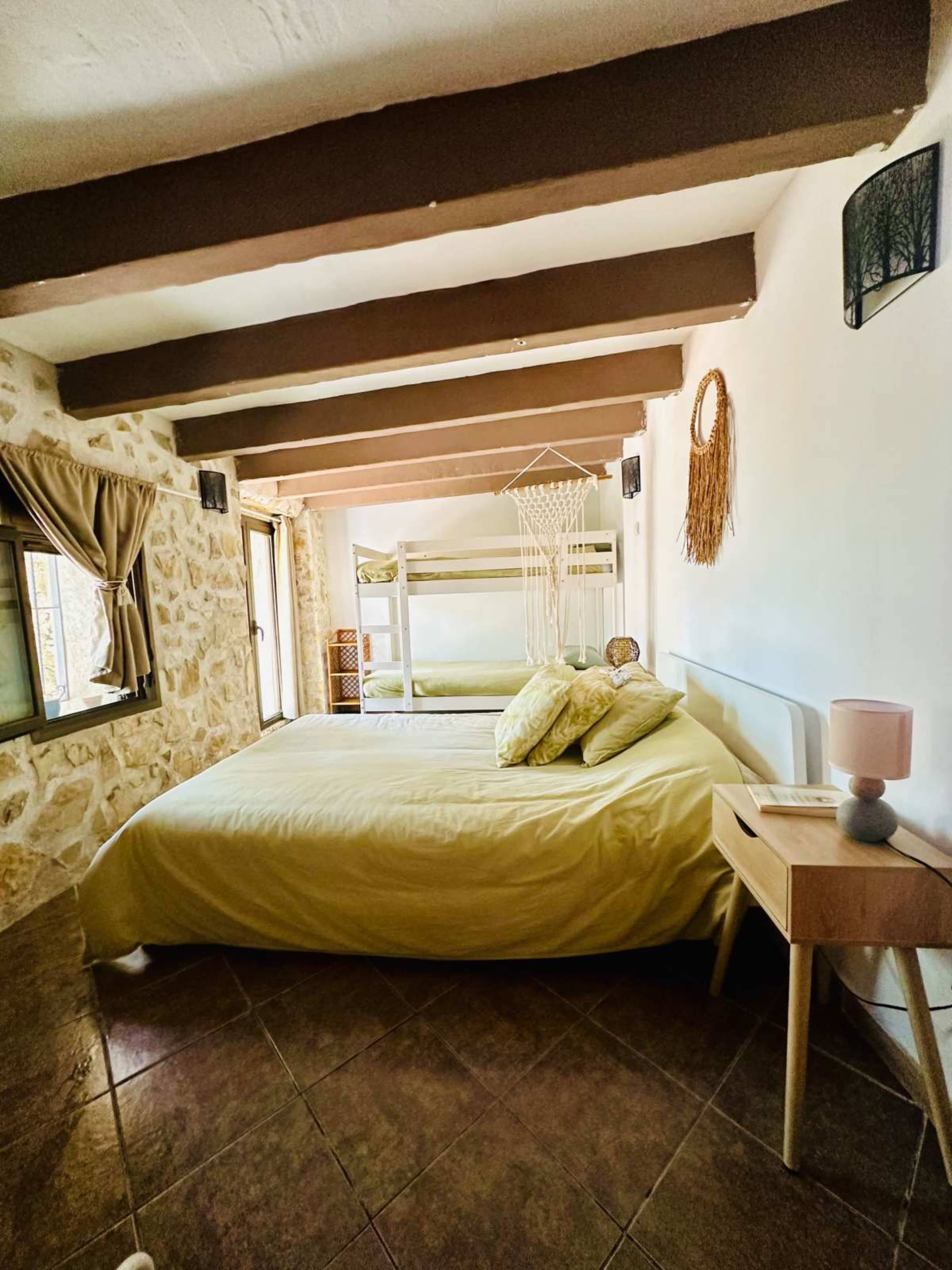 The image shows a cozy bedroom featuring a yellow bedspread, a wooden nightstand with a lamp, and stone walls.
