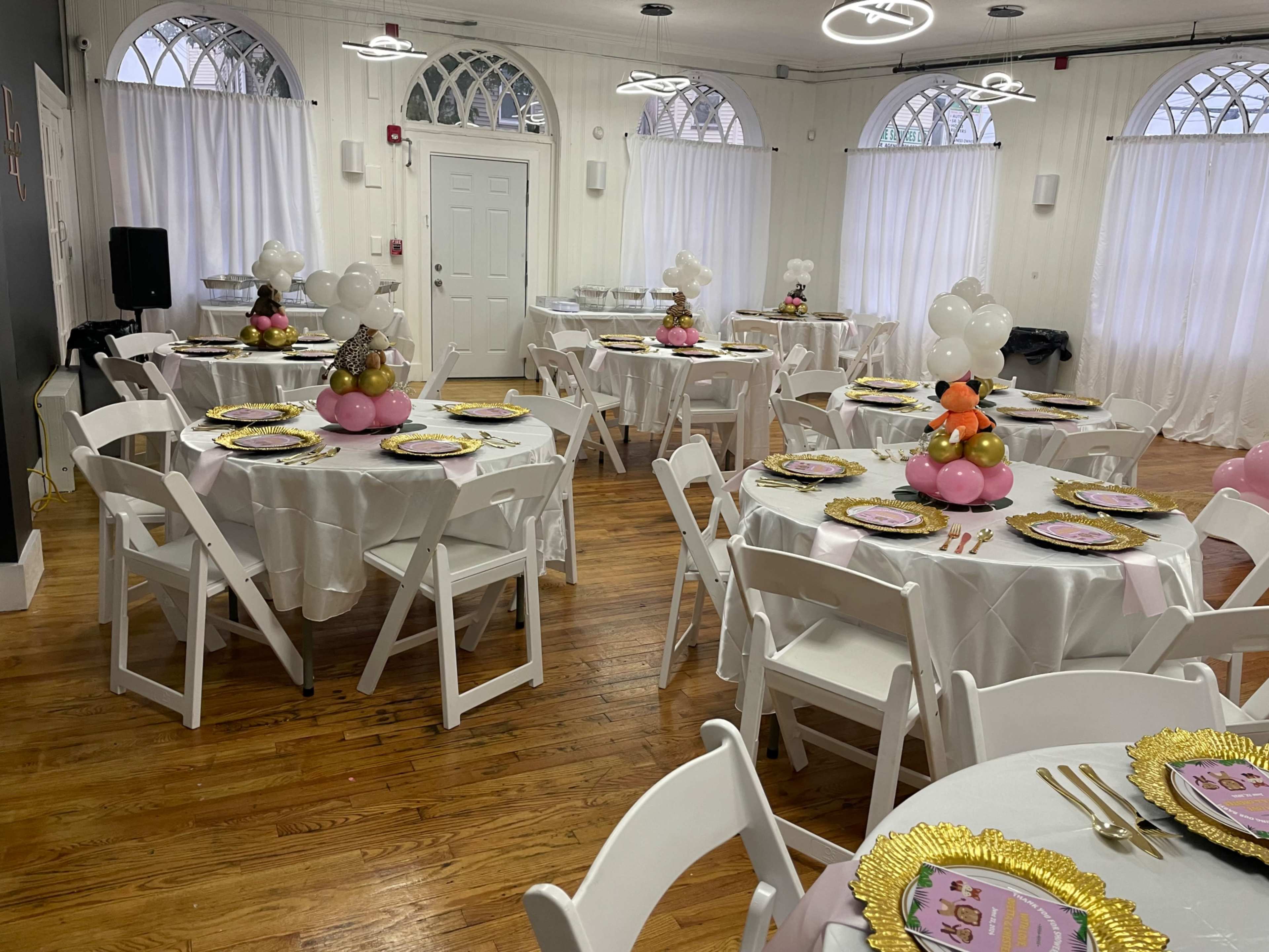 A decorated event space featuring several round tables dressed in white tablecloths, each topped with colorful centerpieces and set with gold-rimmed plates.