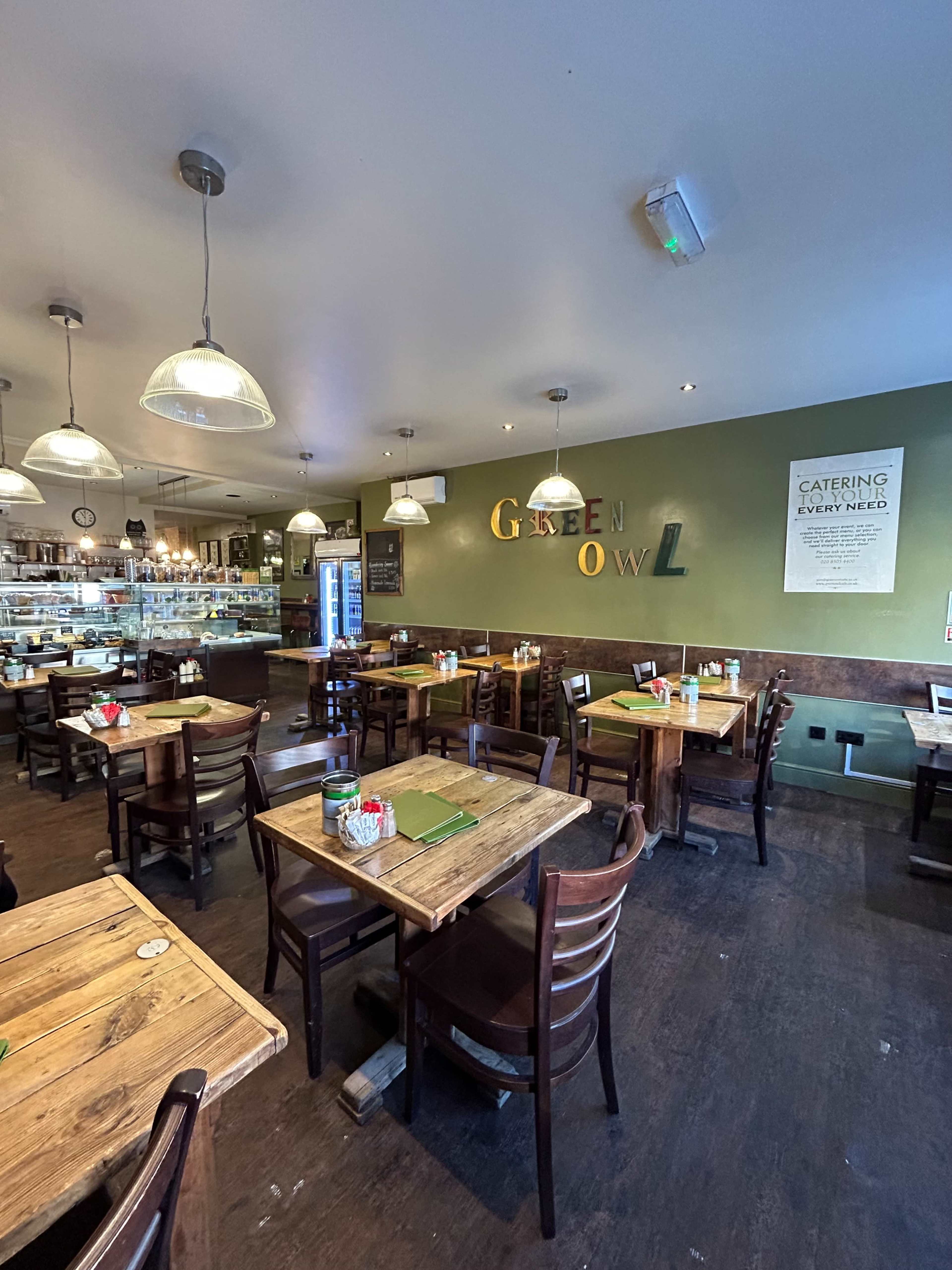 A cozy restaurant interior with wooden tables and chairs, where the words "Green Owl" are displayed on the wall.