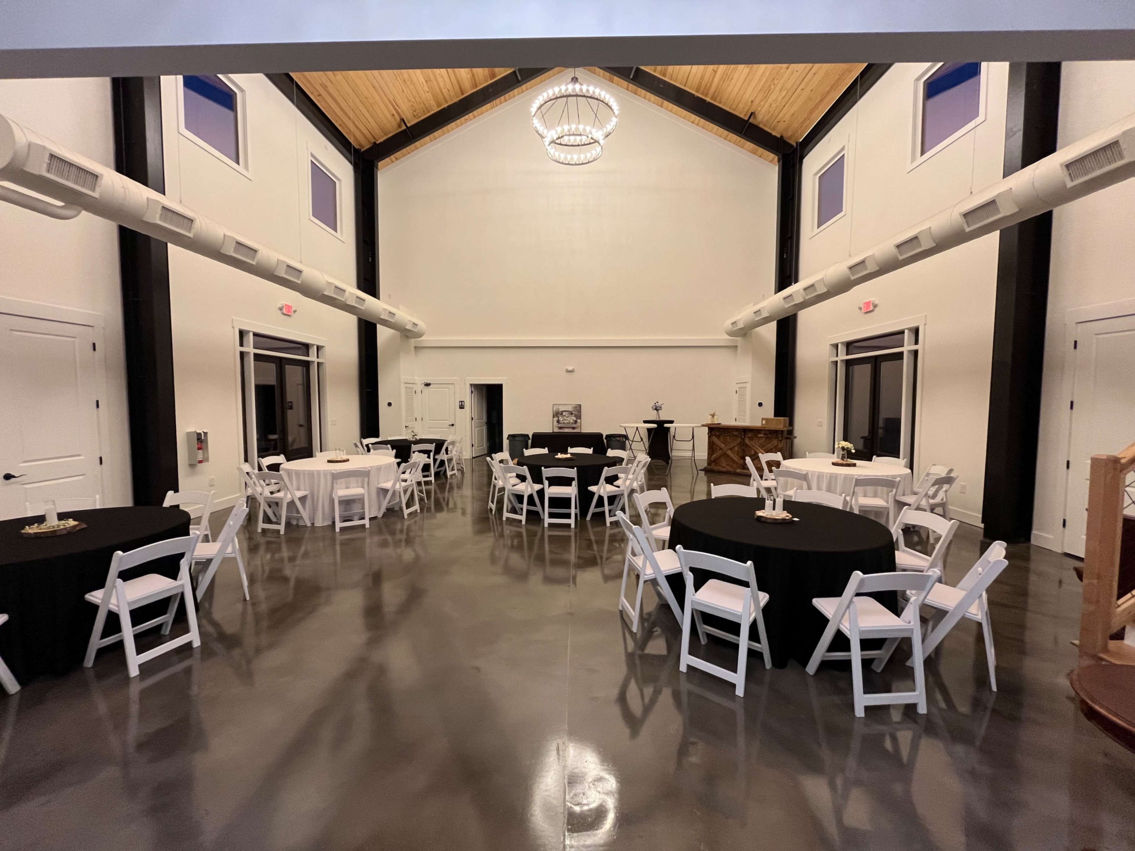 A spacious indoor event hall with round tables dressed in black and white linens, illuminated by a large chandelier.