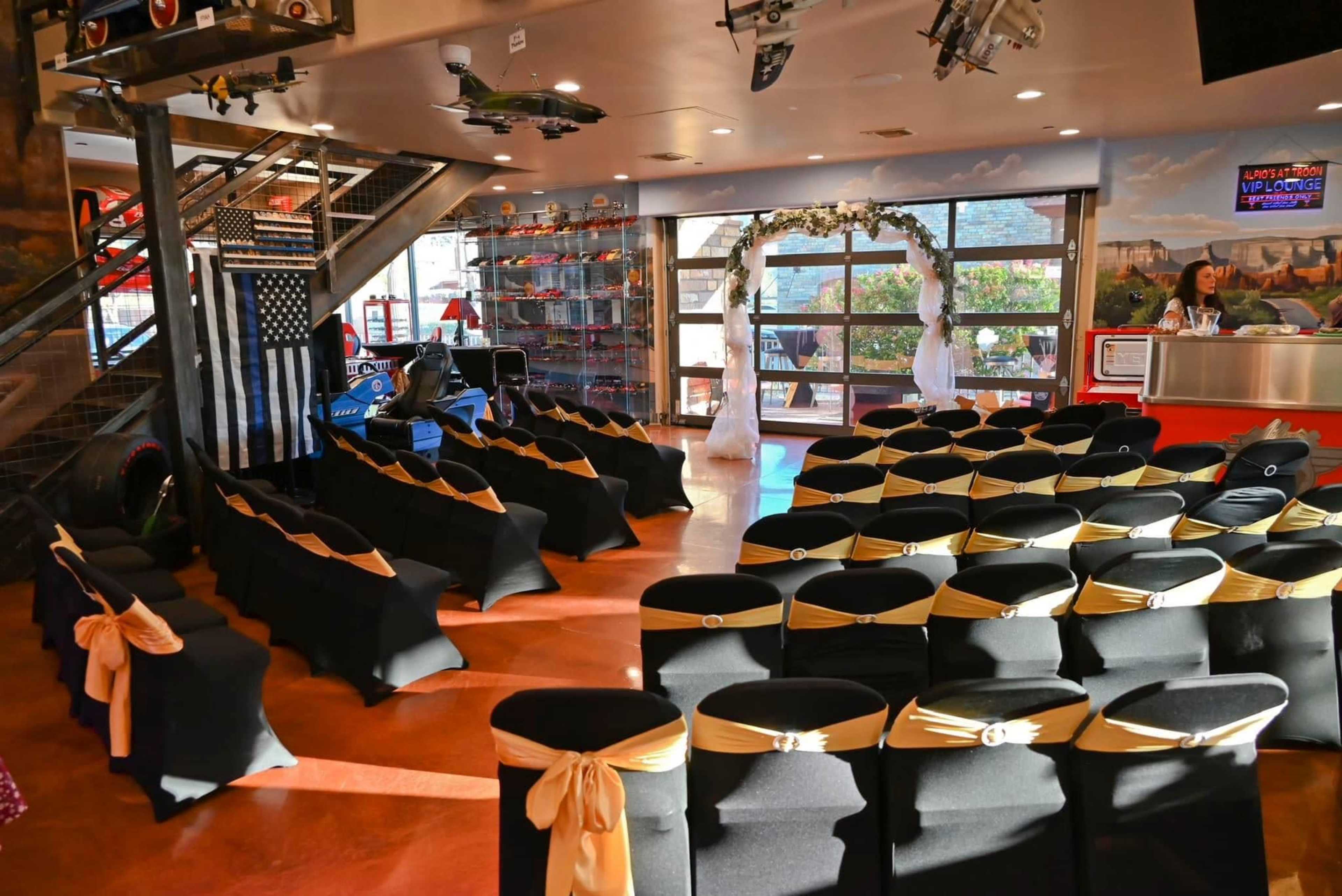 The image shows a neatly arranged event space with rows of chairs covered in black fabric and adorned with gold sashes, set up for a gathering or ceremony.