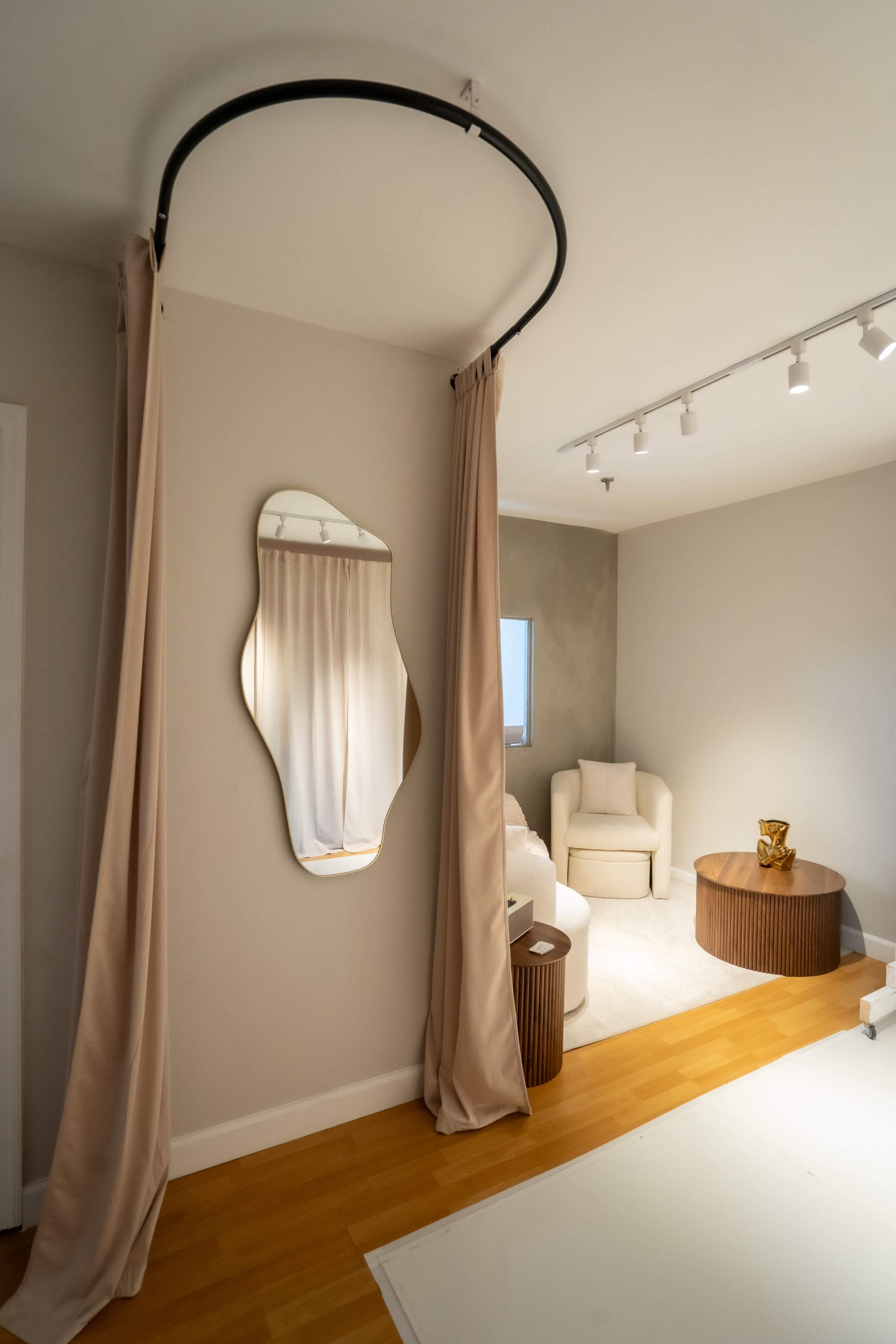 A circular fabric drape hangs from the ceiling beside a mirror, with a cozy seating area and a round wooden table in the room.