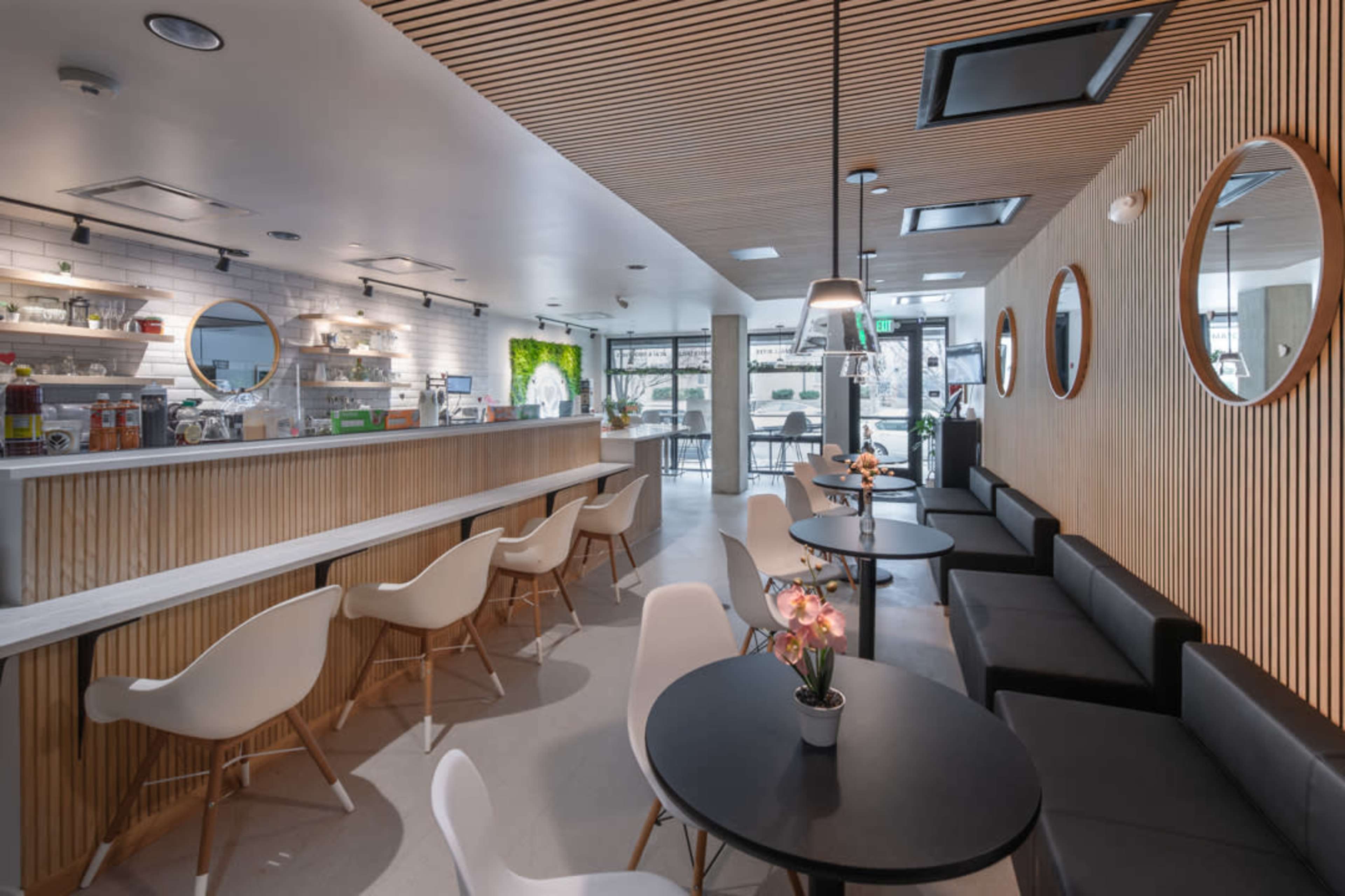 The image shows a modern café interior featuring wooden accents, circular mirrors, white chairs, and round black tables.