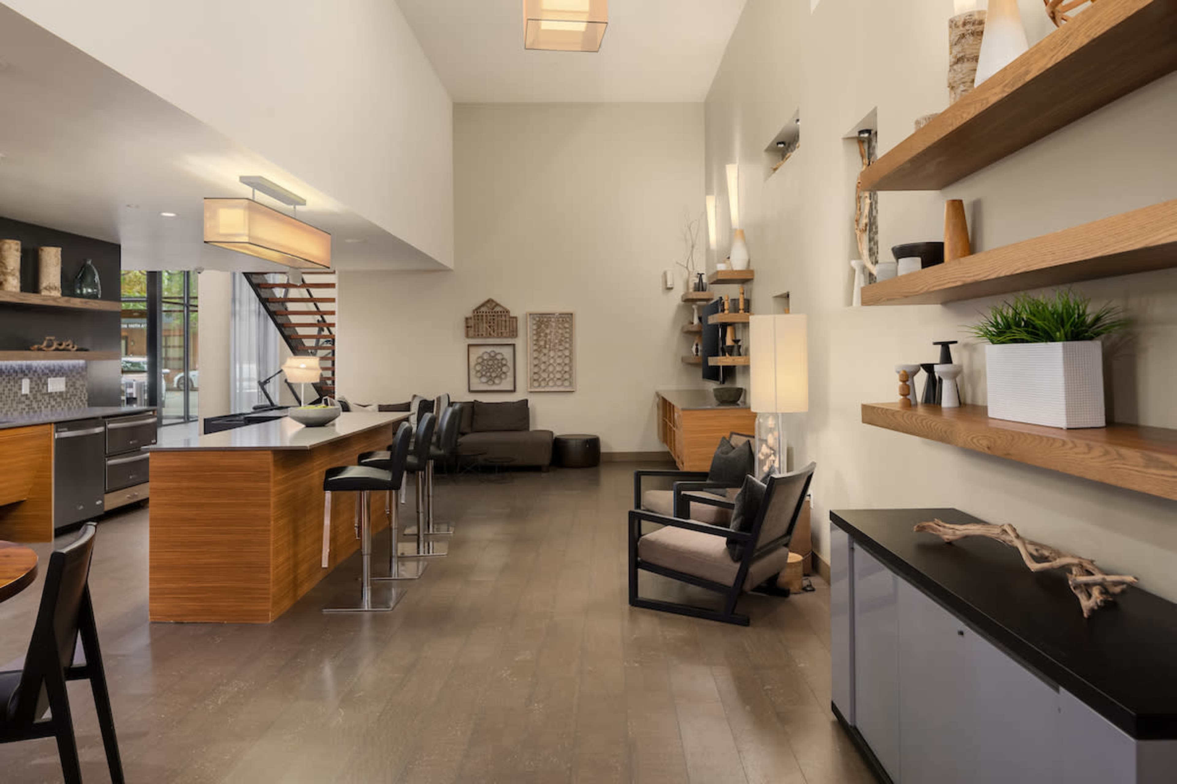 The image shows a modern kitchen and living area with wooden shelves, a dining table, and seating arrangements in a spacious layout.