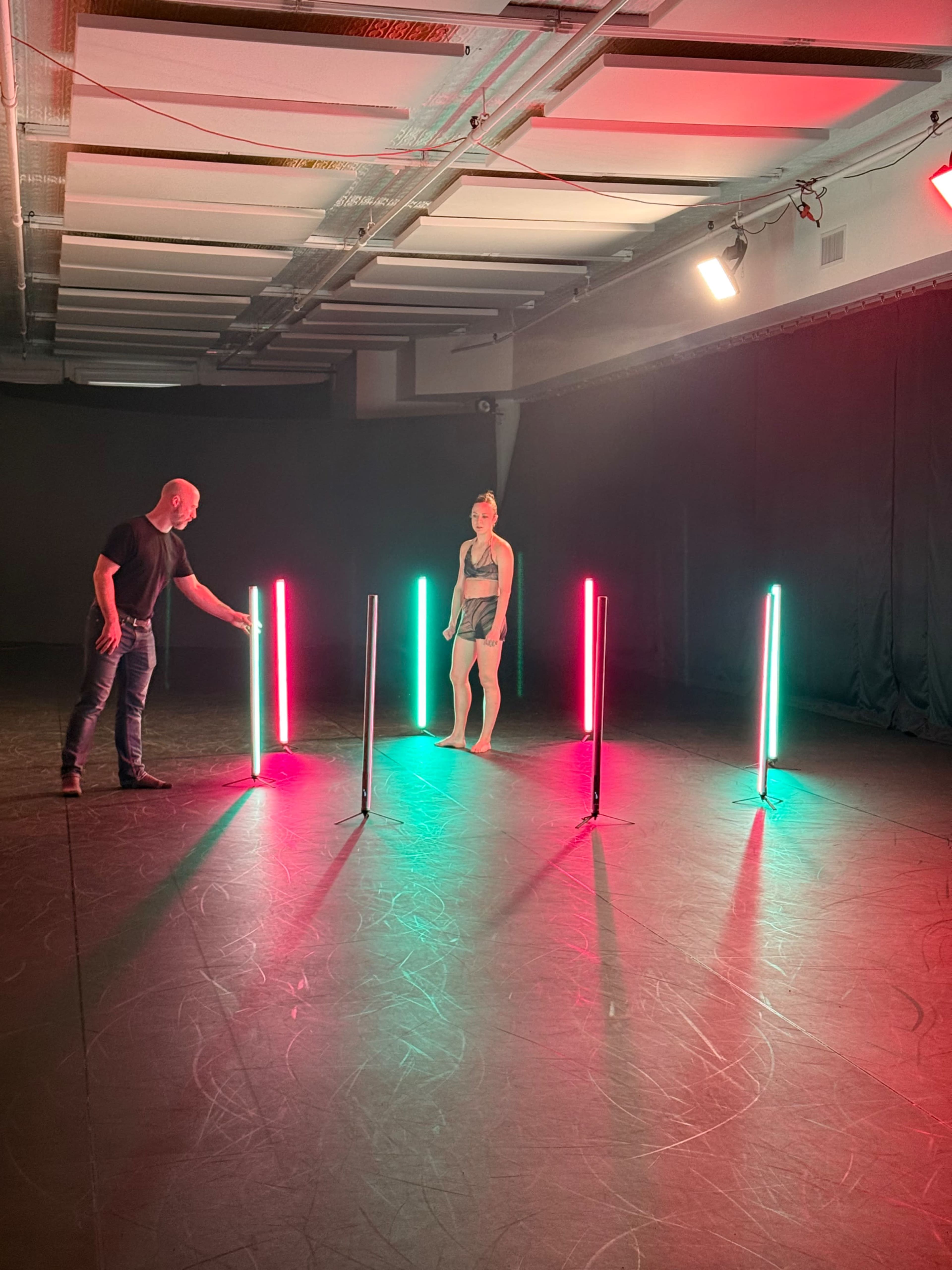 A person stands on a dark stage surrounded by brightly colored vertical light bars.