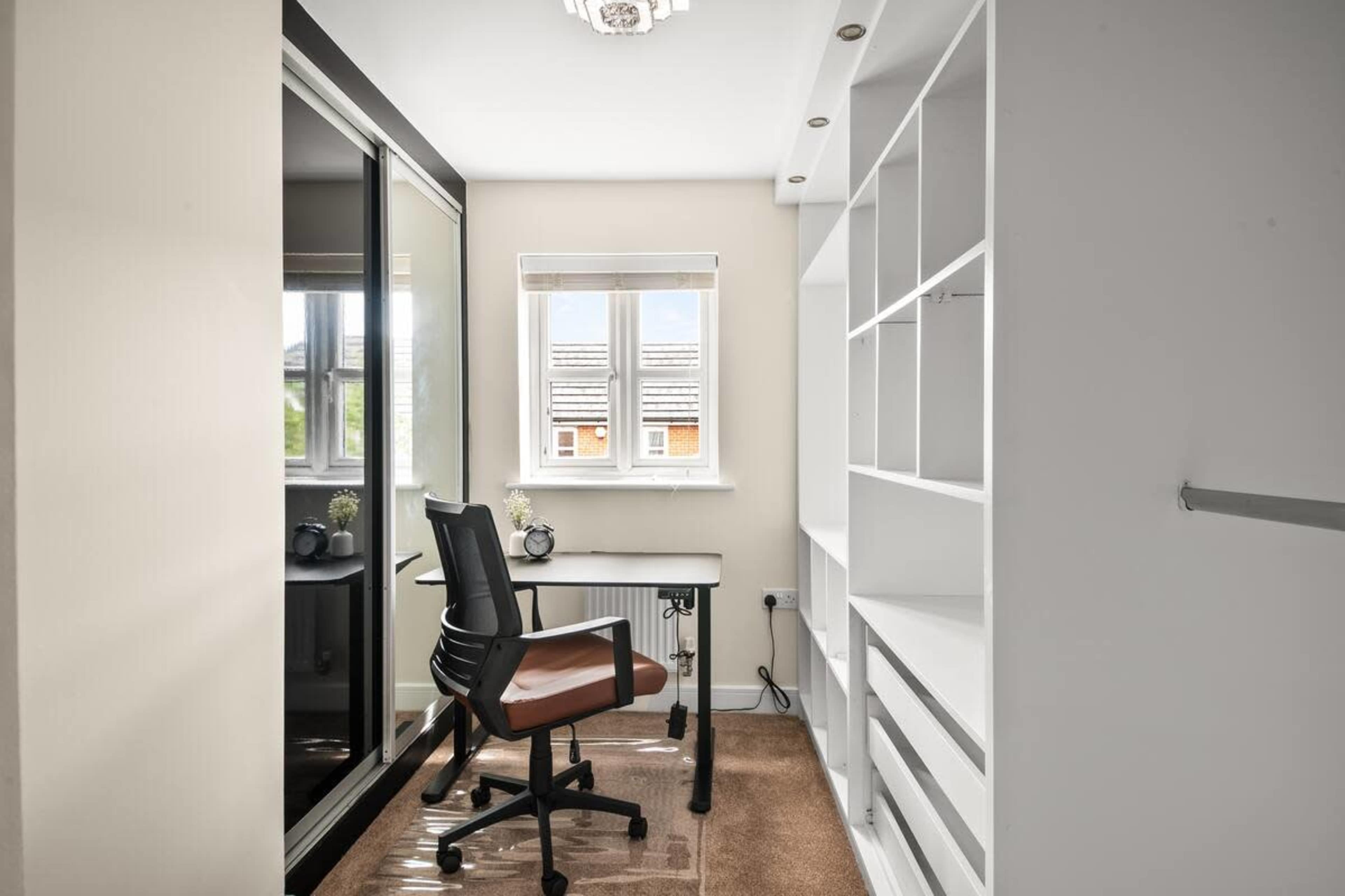 A small office space features a desk with a chair, built-in shelves, and a large mirrored wardrobe.