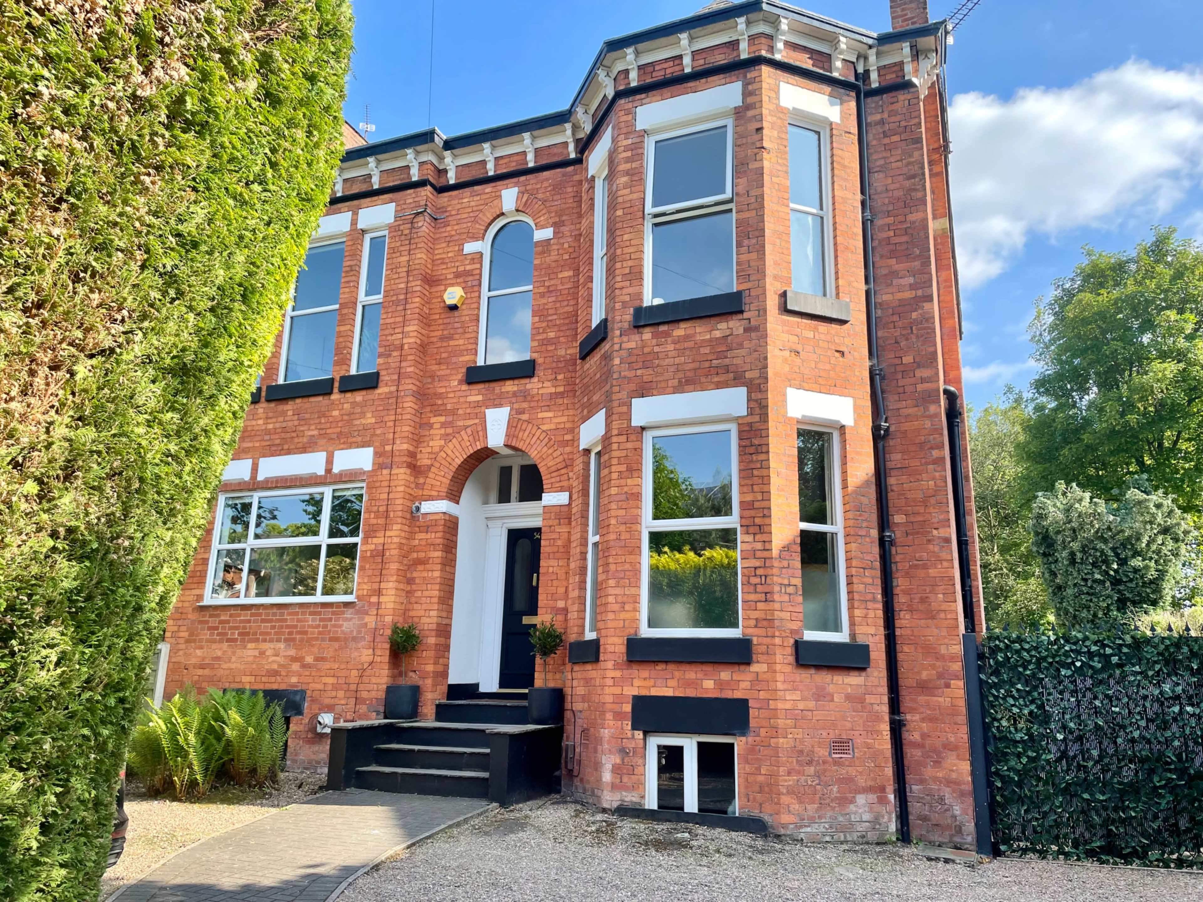 A red brick house with large windows, a symmetrical facade, and a front staircase leading to the entrance.