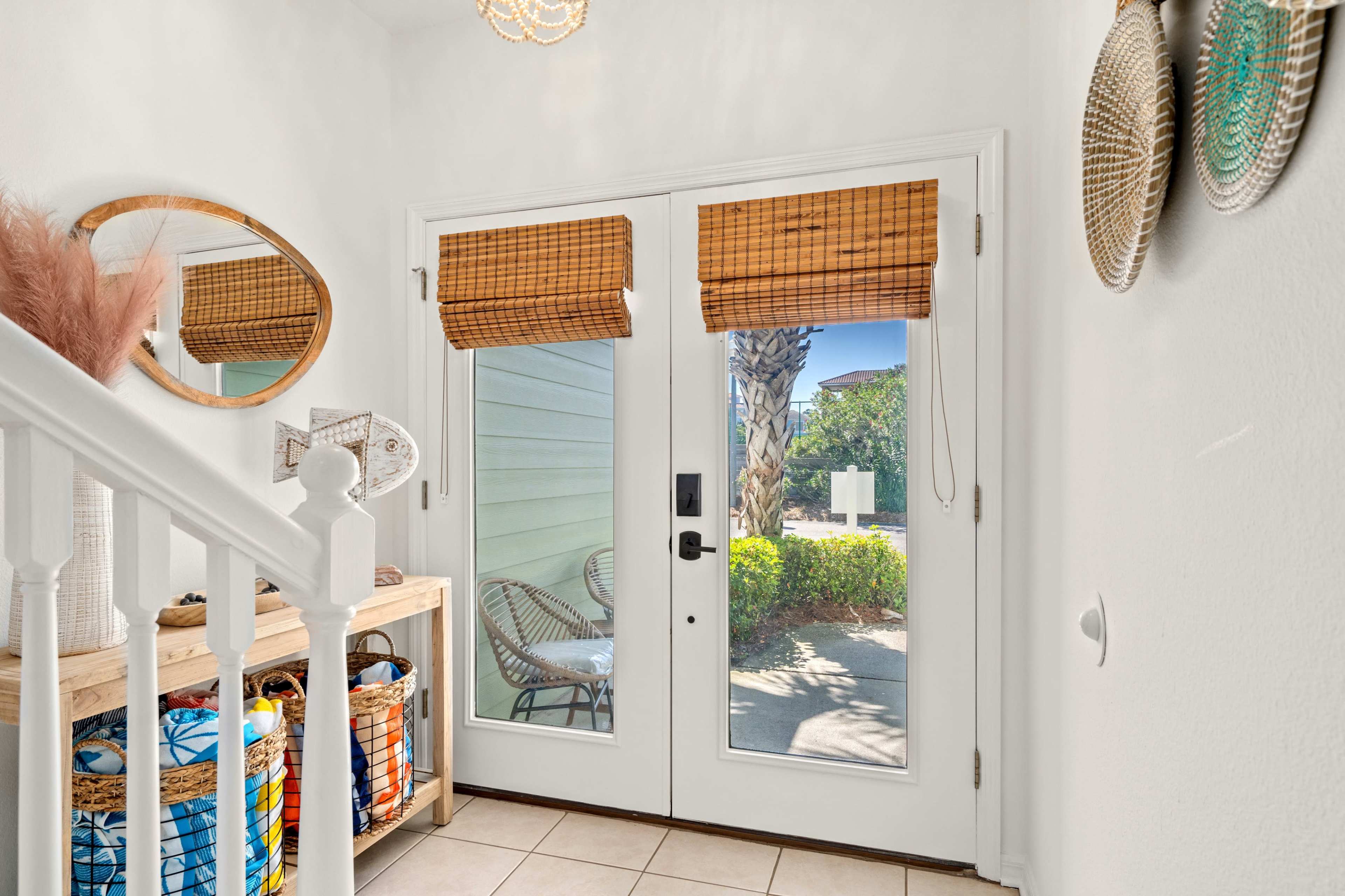 A bright entryway with double glass doors, bamboo shades, and a wooden console table adorned with decorative baskets.