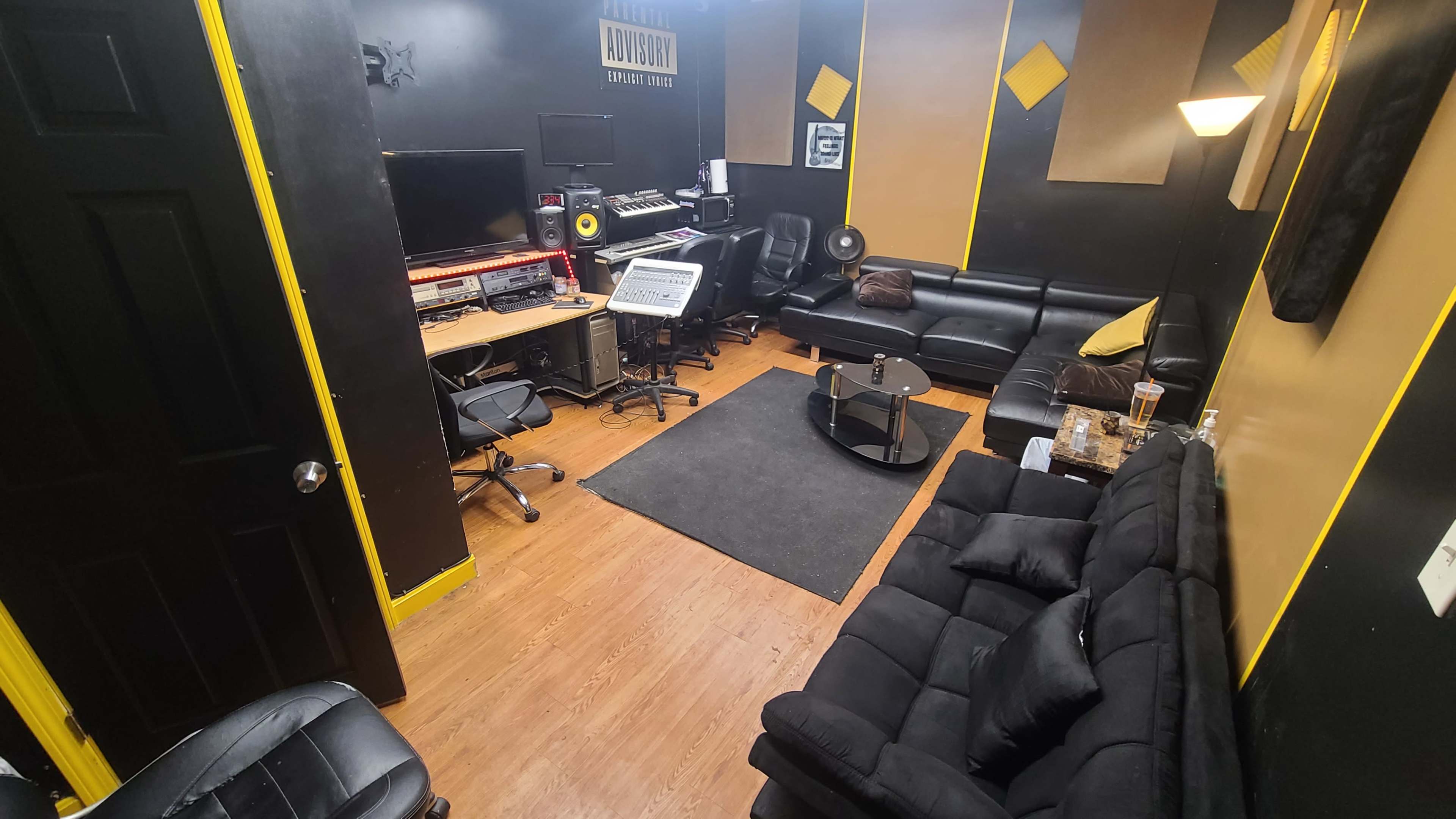 A recording studio with black sofas, a computer workstation, and sound equipment arranged in a compact space.