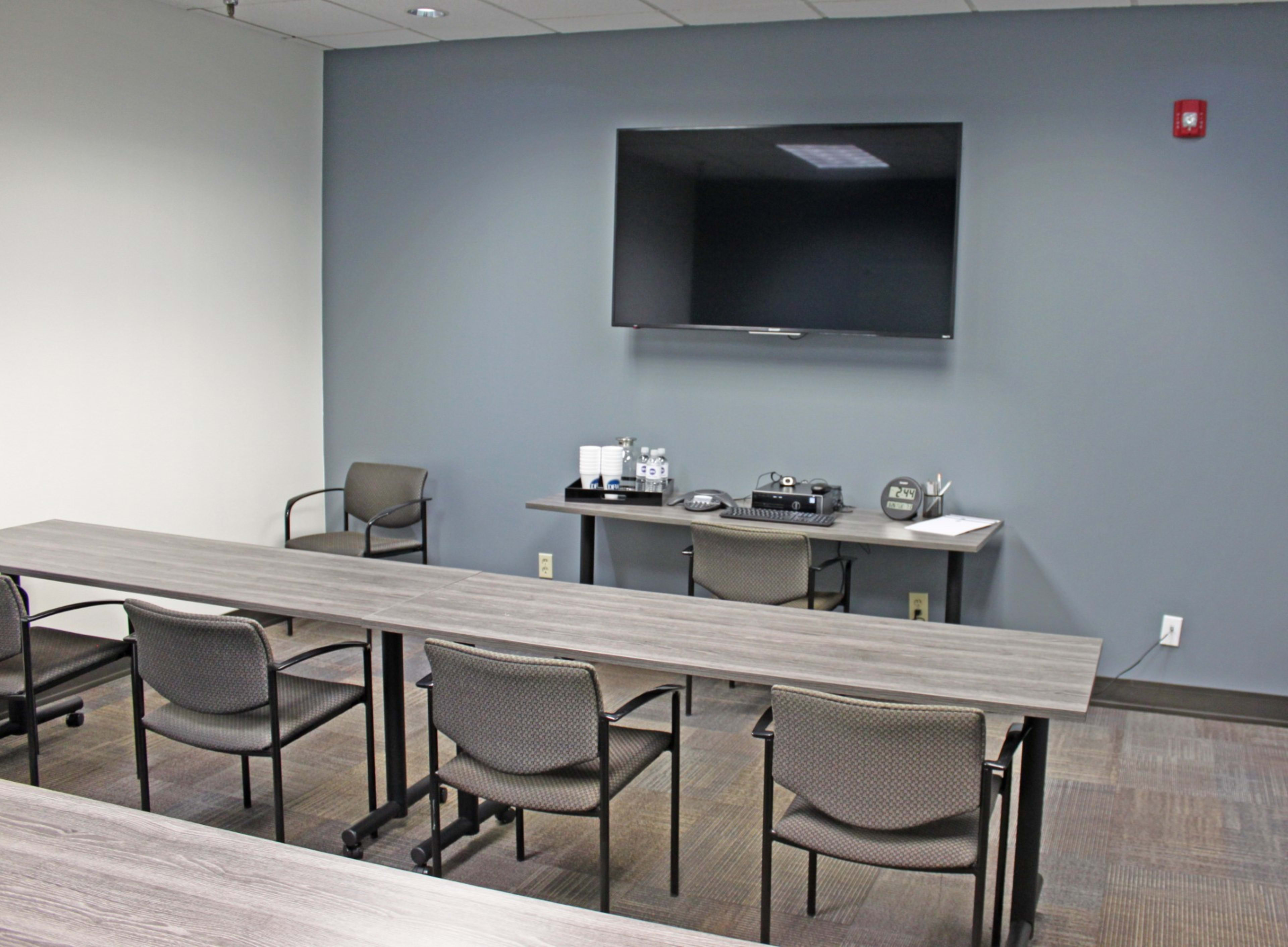 A conference room features a long table, several chairs, and a wall-mounted television.