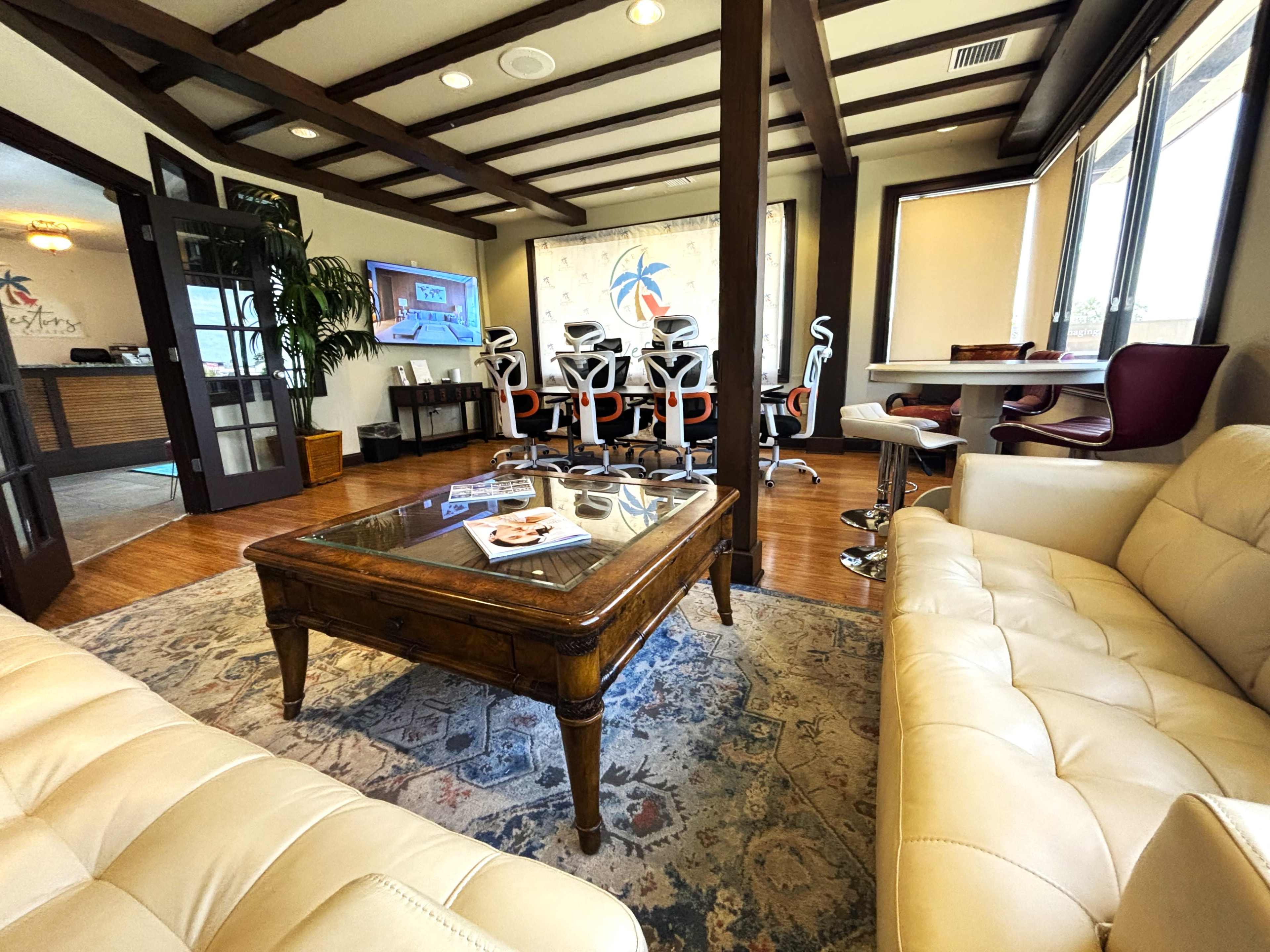 The image shows a modern office waiting area with a beige leather couch, a wooden coffee table, and a conference table surrounded by ergonomic chairs.