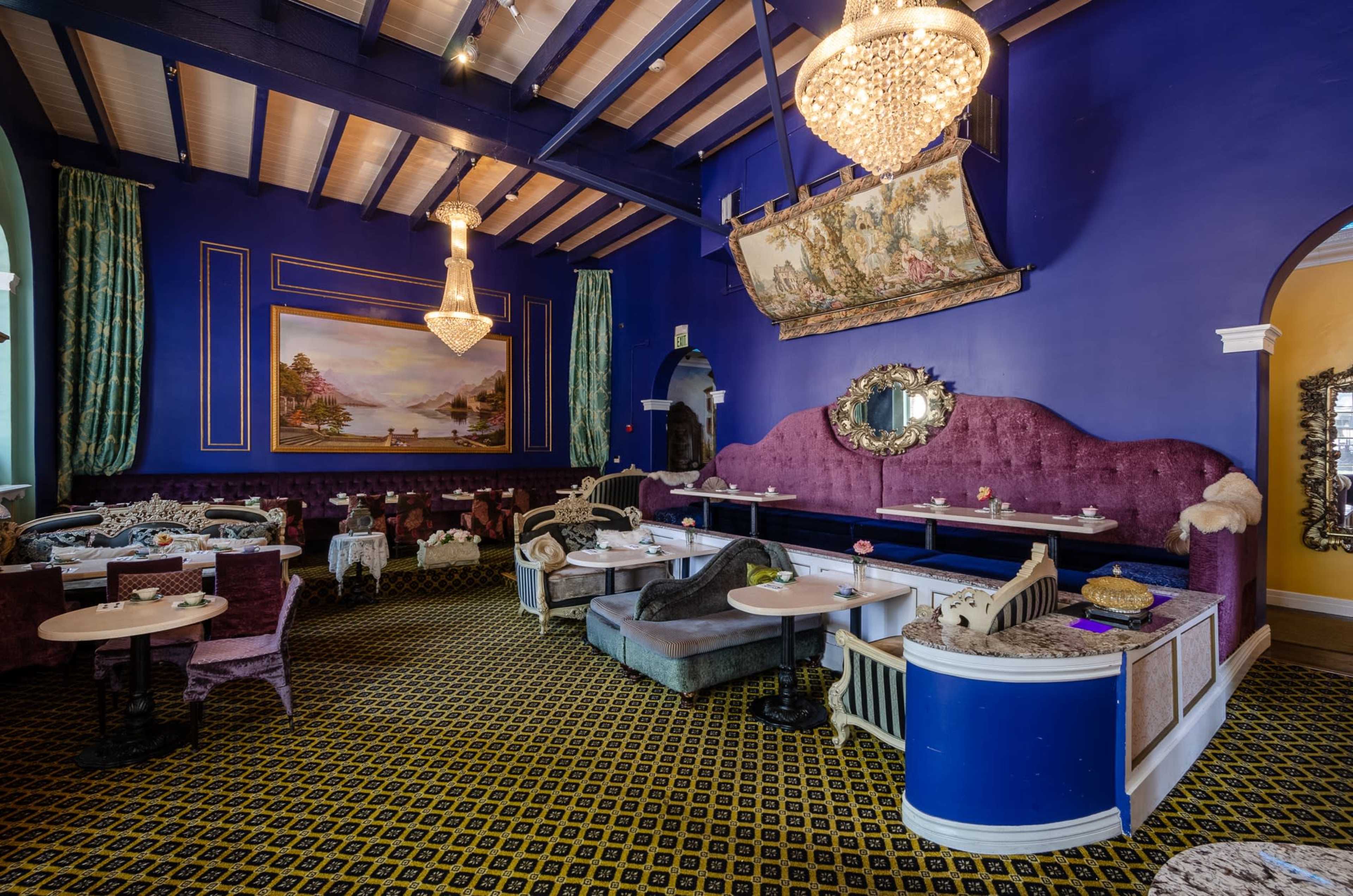 The image shows a vibrant restaurant interior with purple seating, ornate chandeliers, and decorative art on the walls.