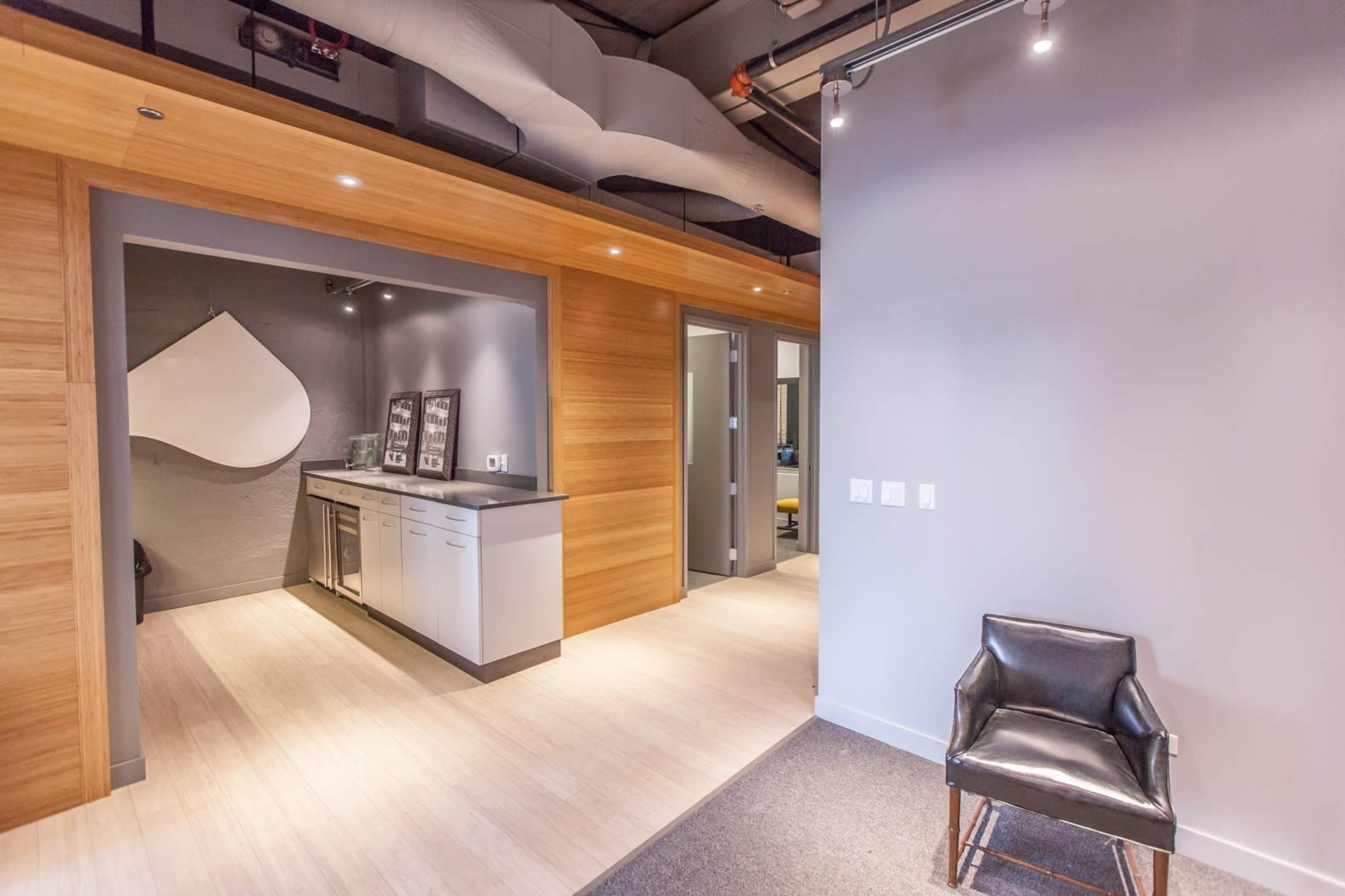A modern office space with a wooden-paneled entrance, a kitchenette area, and a black chair placed beside a wall.