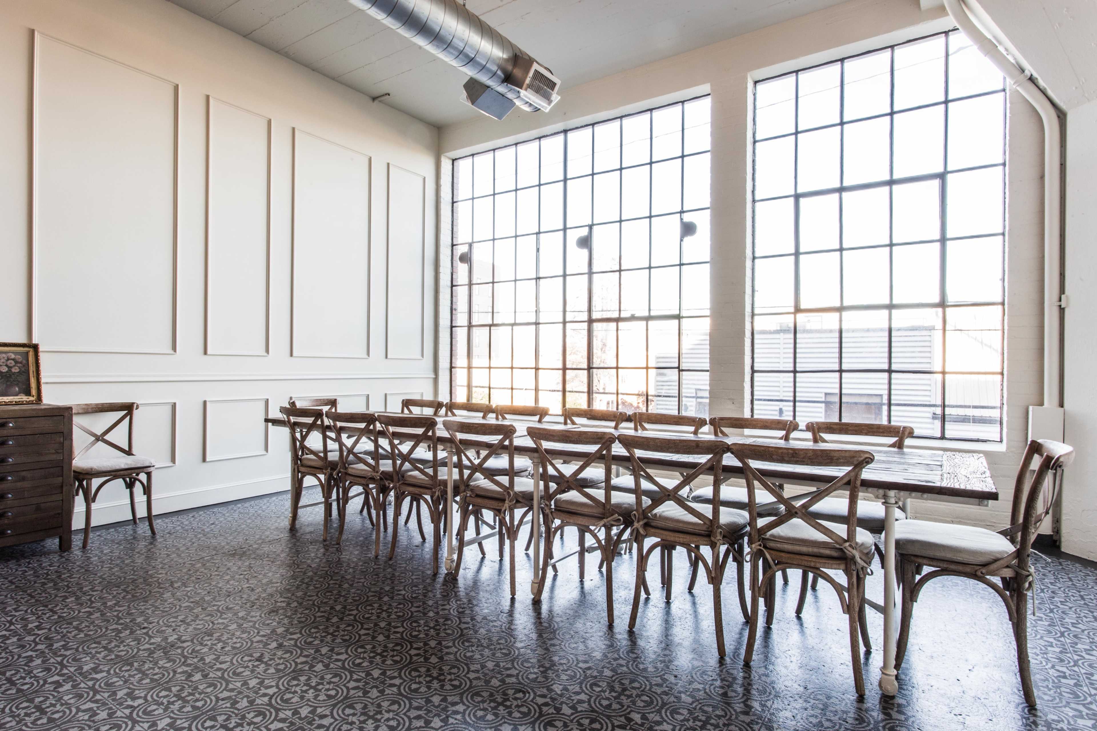 A spacious dining room features a long wooden table and chairs, with large windows allowing natural light to fill the area.