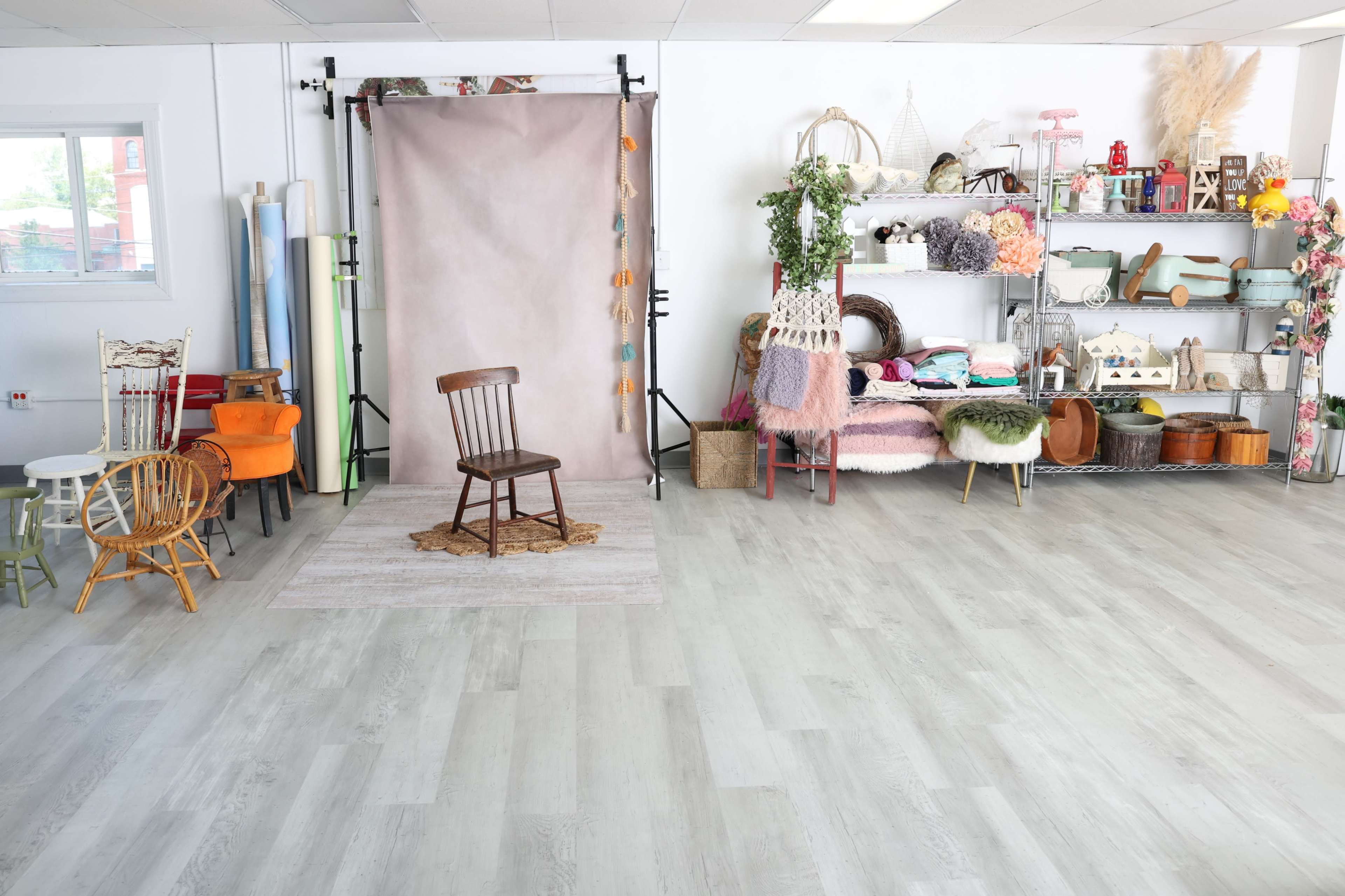 A bright studio space featuring a simple wooden chair at a backdrop, with various decorative items and props neatly arranged on shelves to the right.