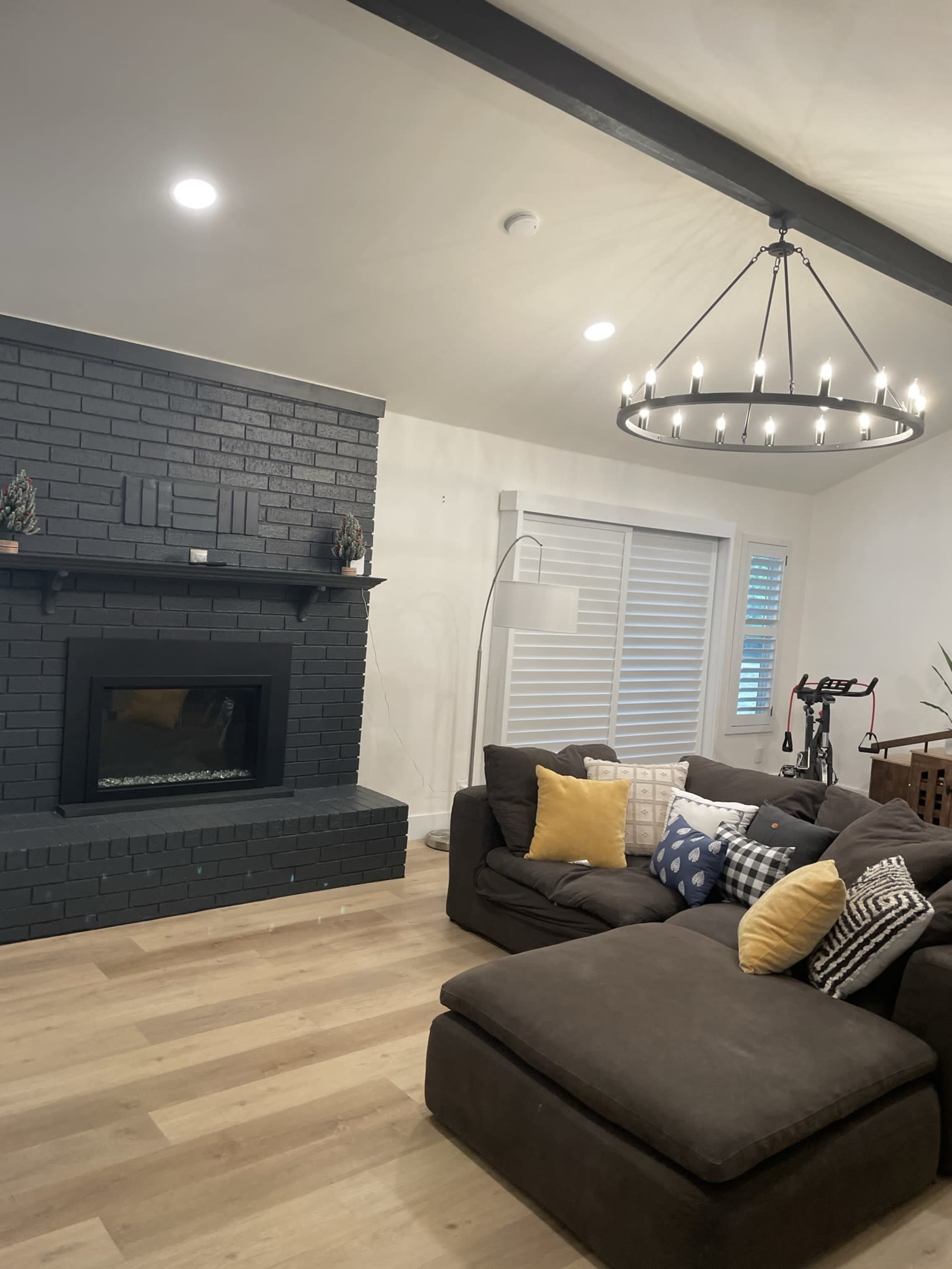 A living room featuring a dark brick fireplace, a large sectional sofa with decorative pillows, and a modern chandelier.