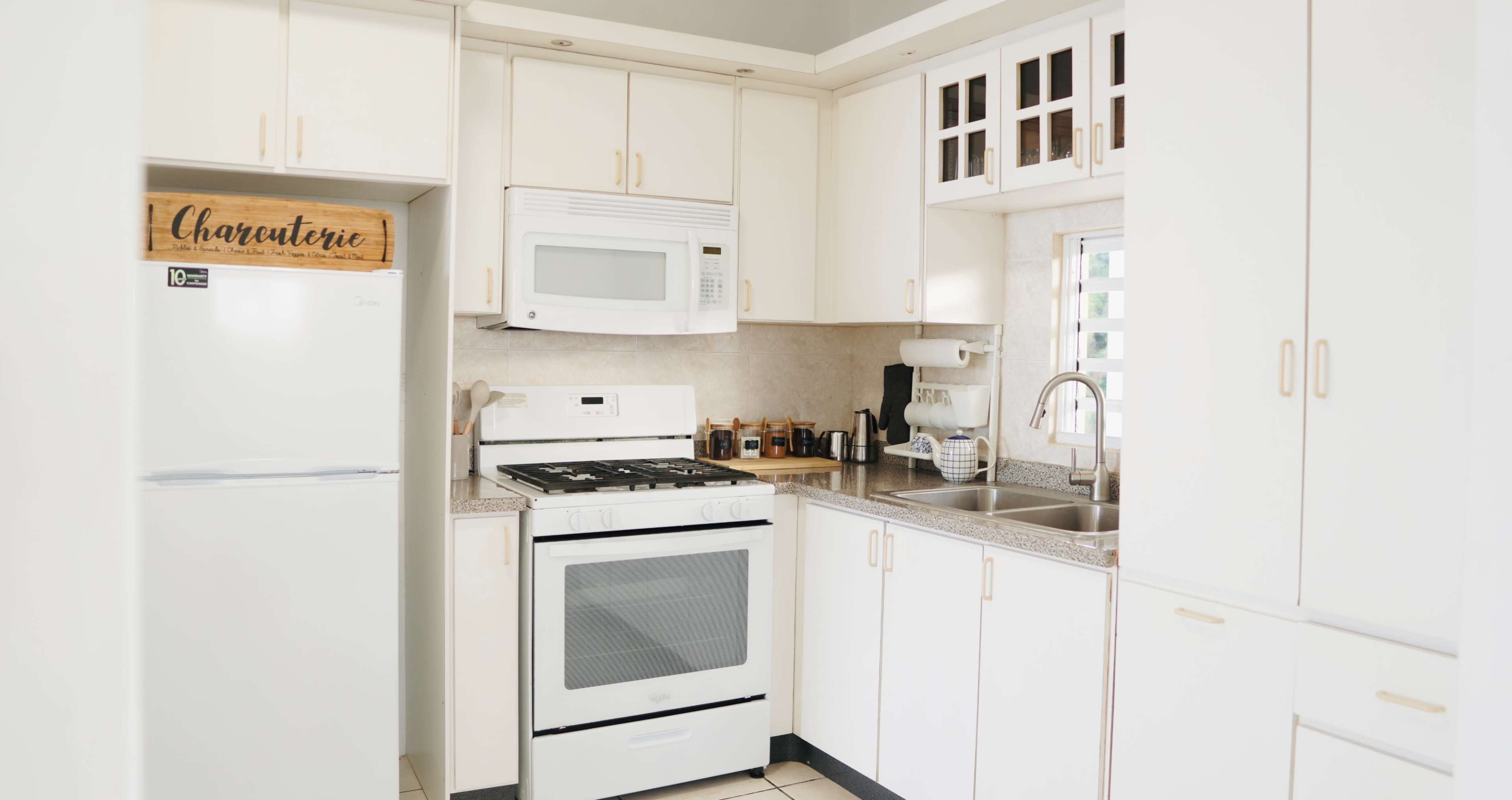 A modern kitchen features white cabinets, a stainless steel sink, a gas stove, a microwave, and a refrigerator.