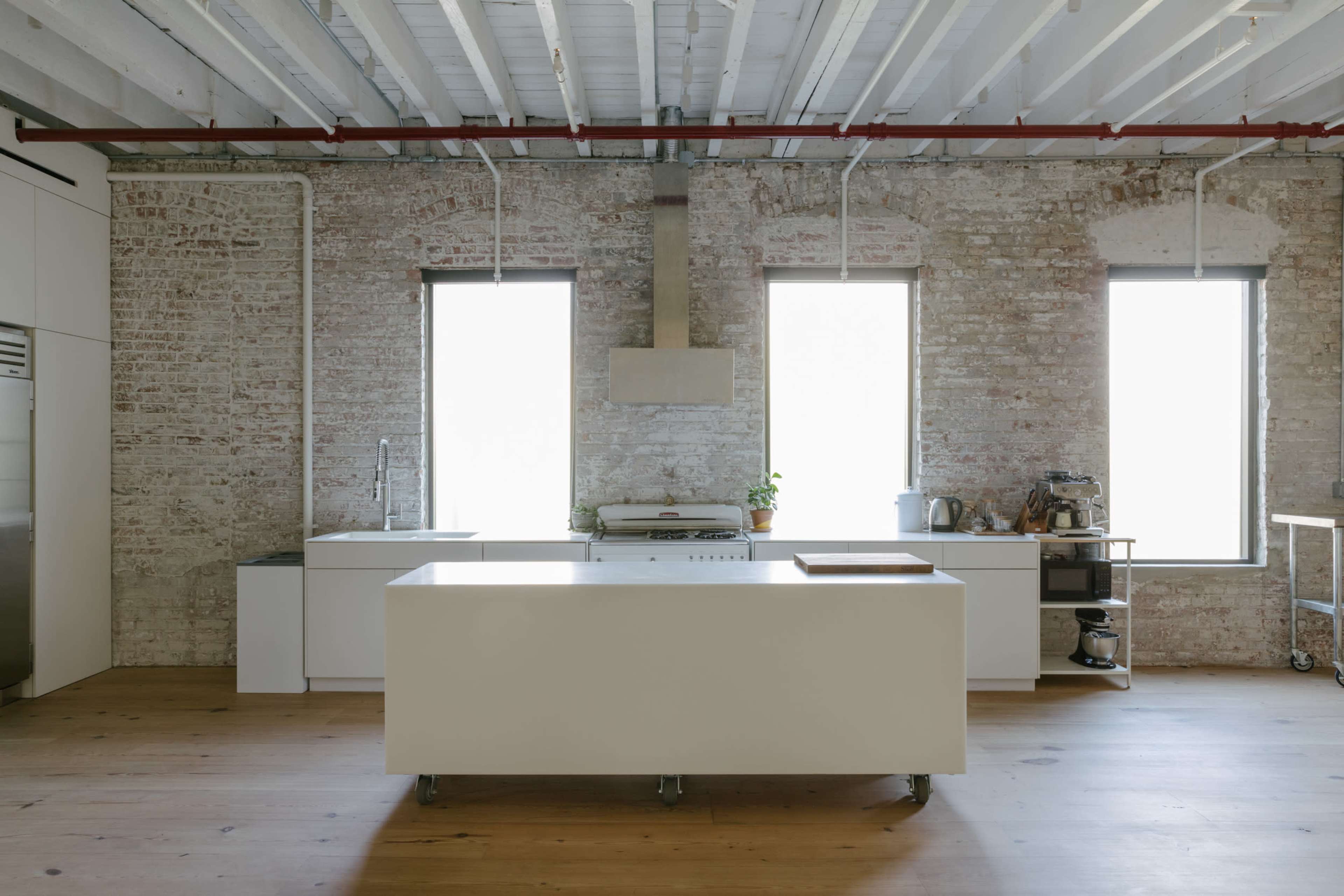 A spacious kitchen with a central island, exposed brick walls, and large windows allowing natural light to fill the room.