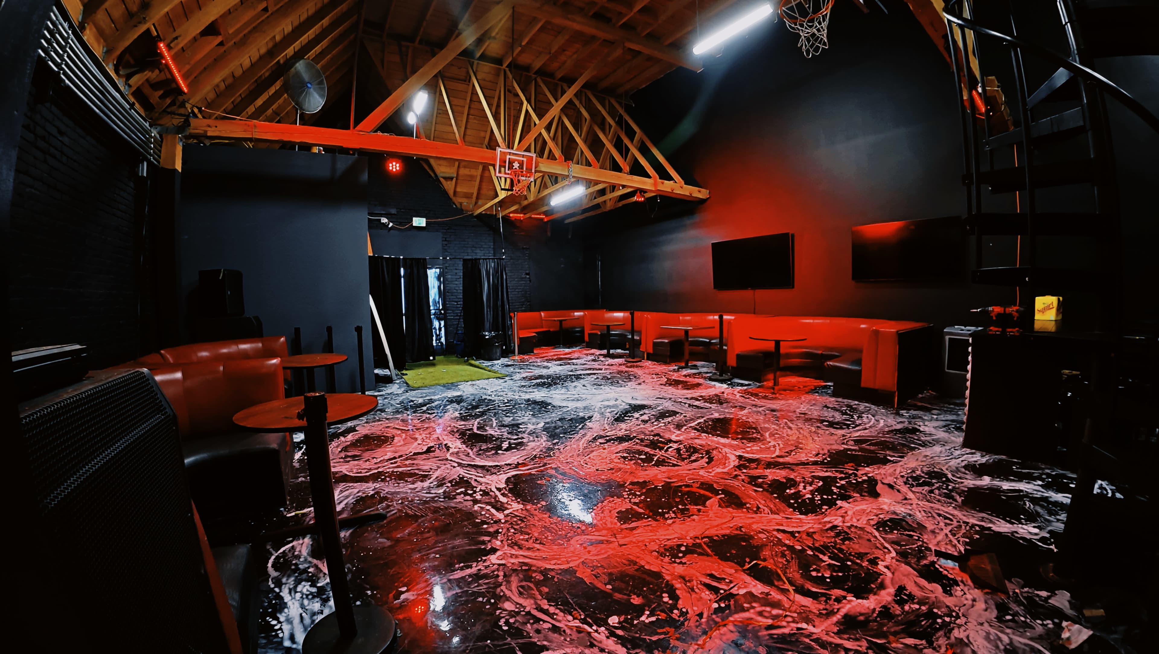 The image depicts a dimly lit room with red lighting, featuring black walls, a polished floor with a swirling white substance, and seating areas along the sides.